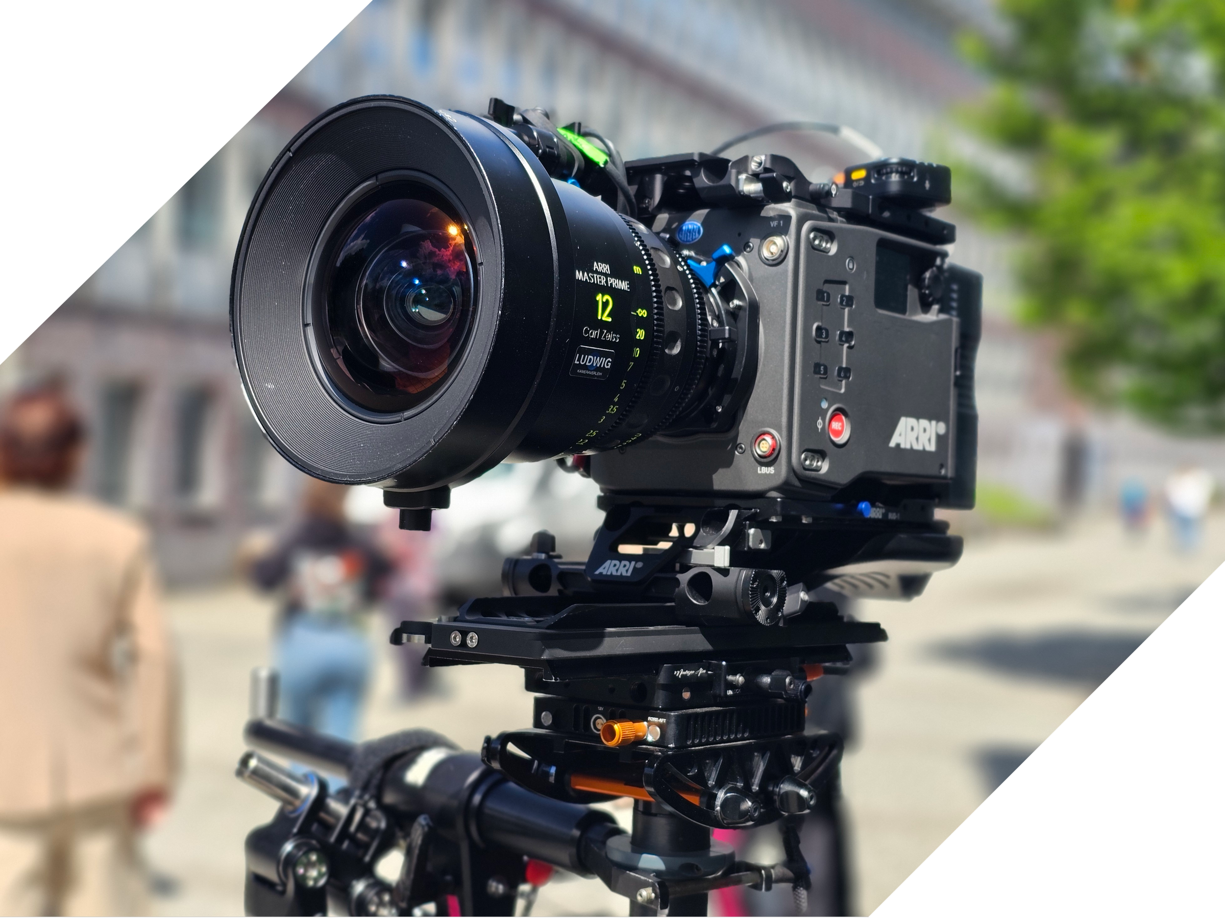 Close-up of professional ARRI camera mounted on a stabilizer in an outdoor setting with blurred people and green trees in the background.