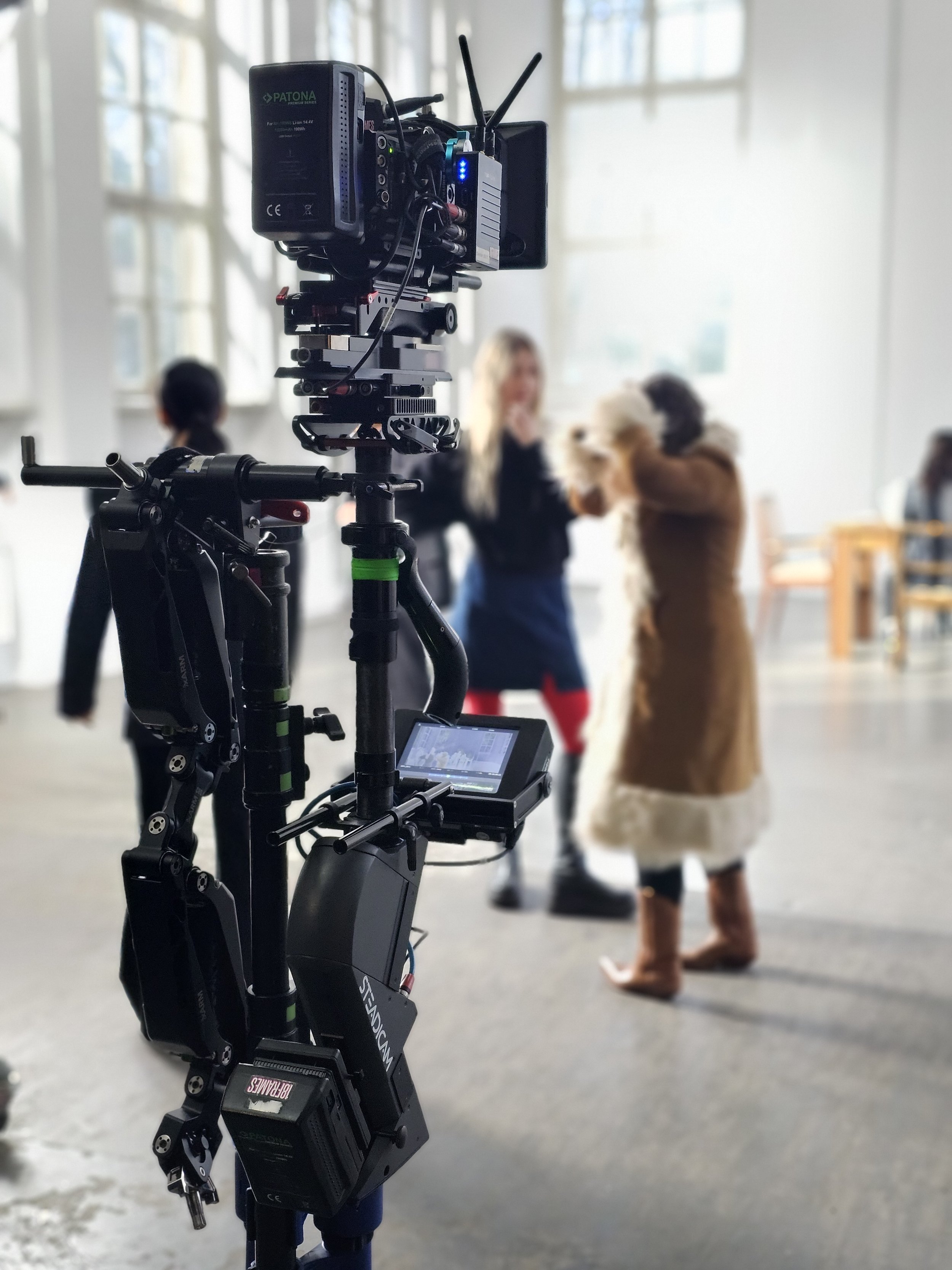 Aufnahmegerät auf einem Stativ in einer Filmproduktionsumgebung, im Hintergrund eine Frau, beim Filmen.