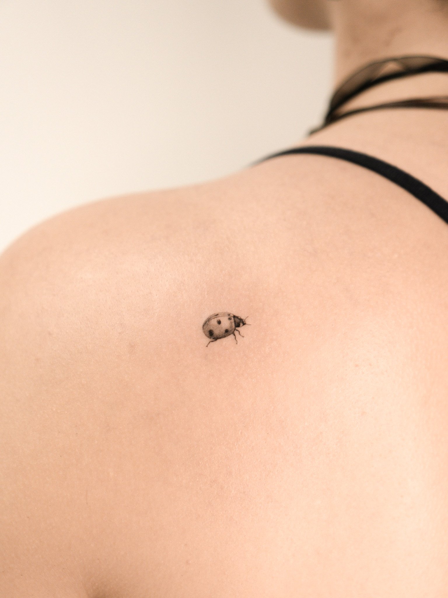 Persona con piel clara lleva ropa interior negra y tiene un tatuaje de una mariquita en el hombro.