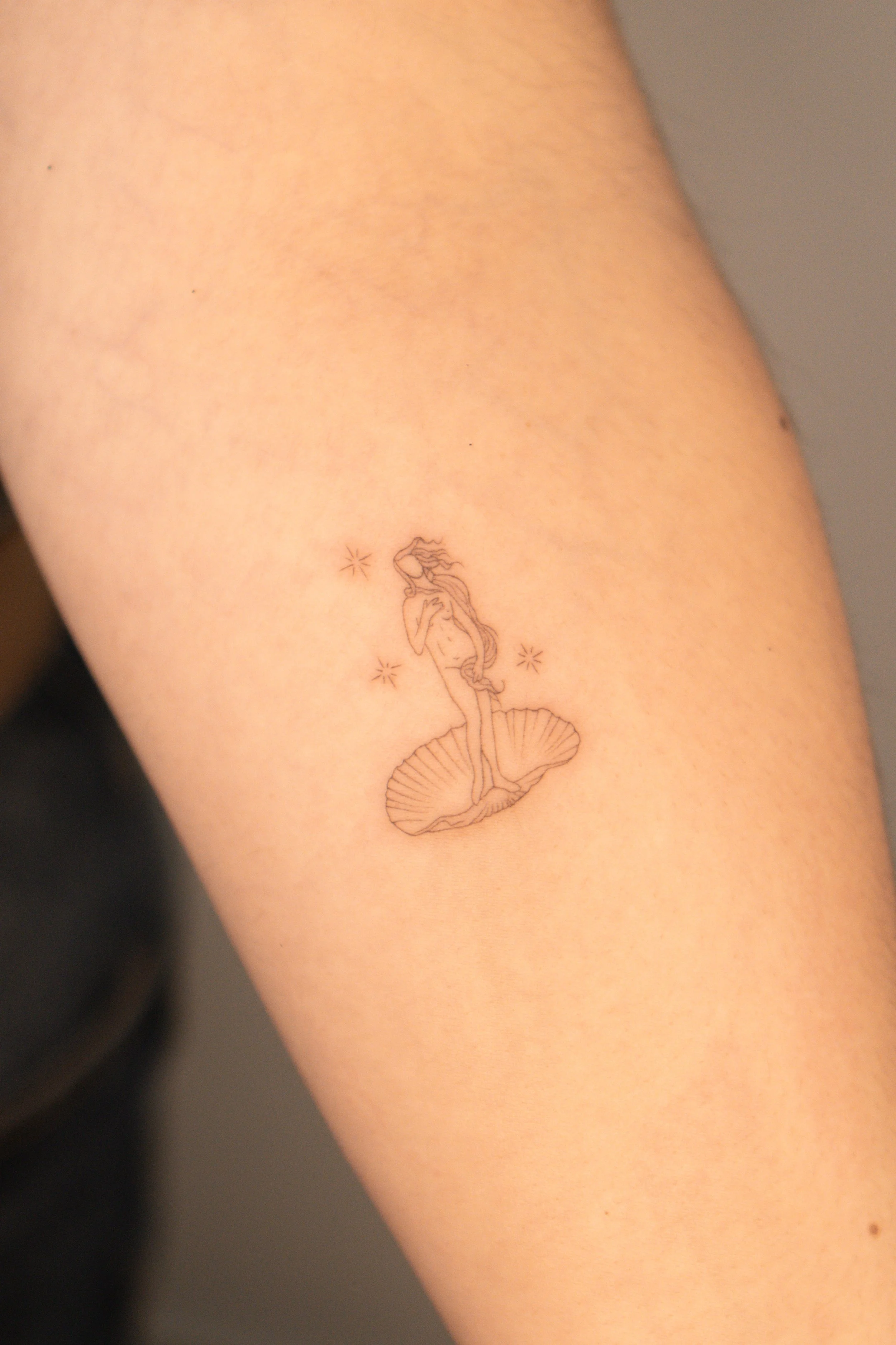 Tatuaje delicado de una sirena sobre un caparazón de concha en el antebrazo