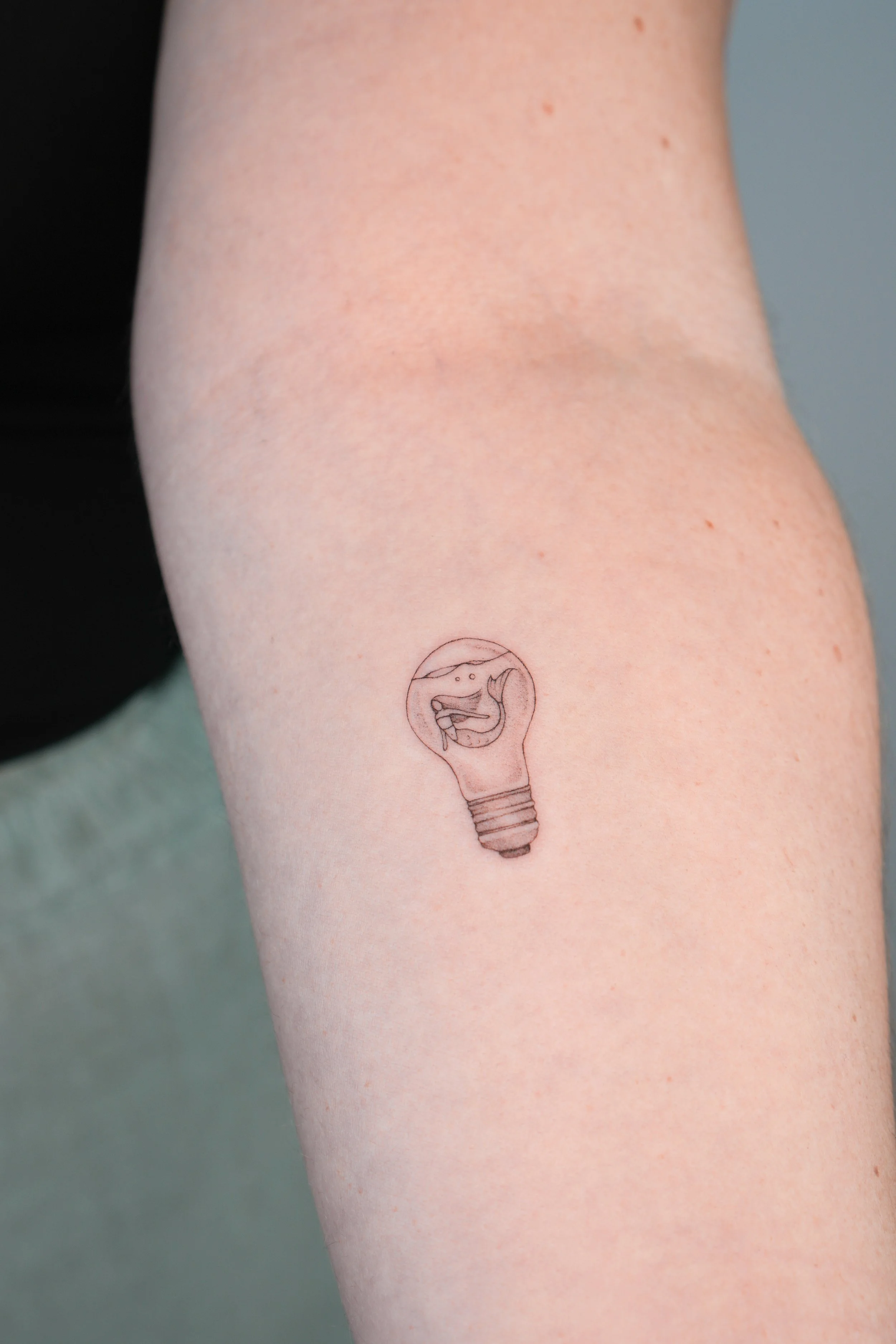 Tatuaje en forma de bombilla con un pez nadando en el interior.