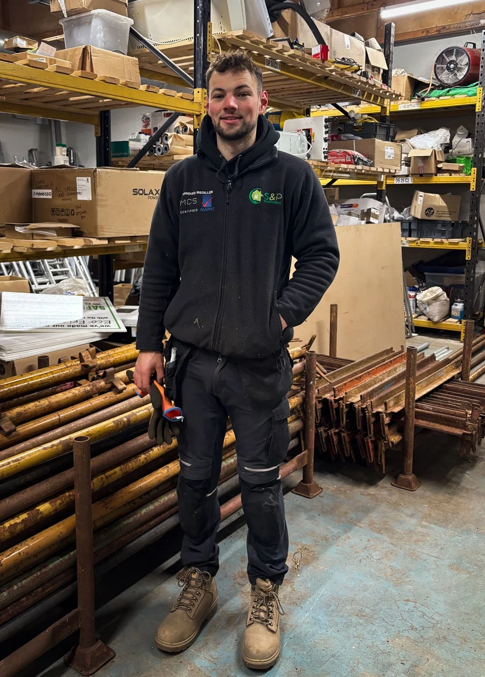 Sam, solar panel installer at s&p renewables Galashiels, standing in a workshop surrounded by solar panel equipment
