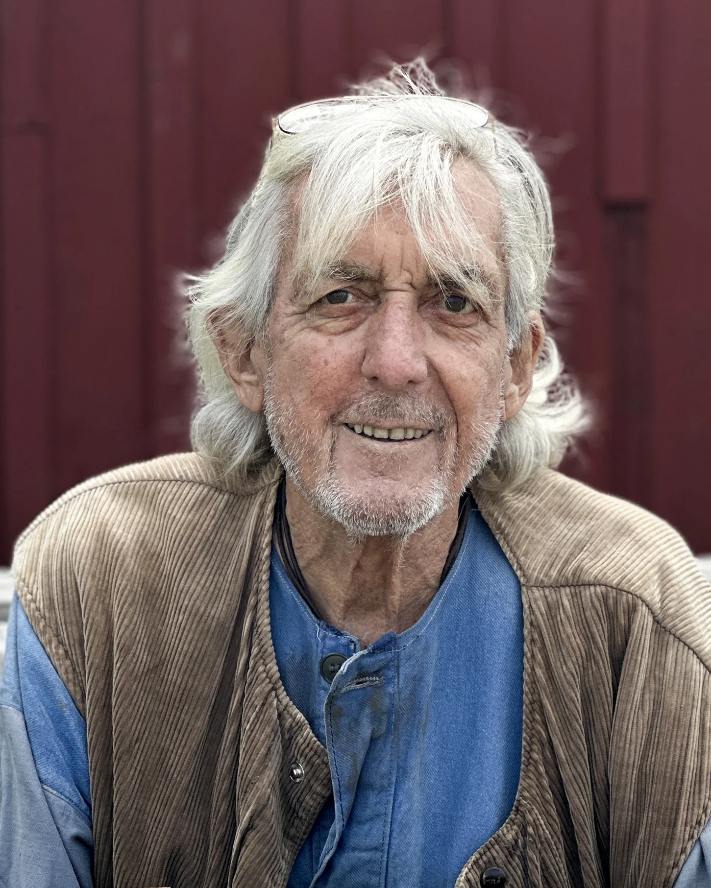 gotland pictures film casting - an older man with white hair and thin beard smiles to the camera. He has jeans shirt underneath a cordoroy vest