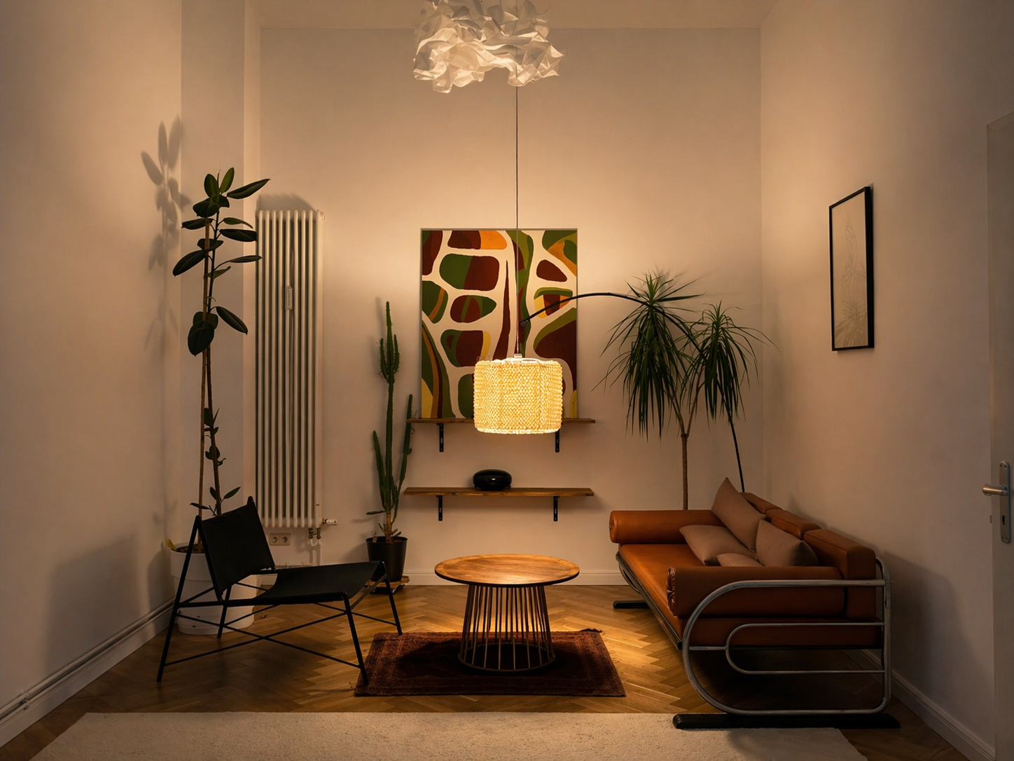 Living room with a brown leather sofa, black chair, round wooden coffee table, tall potted plants, wall art, and a pendant light, with a white wall and wooden floor.
