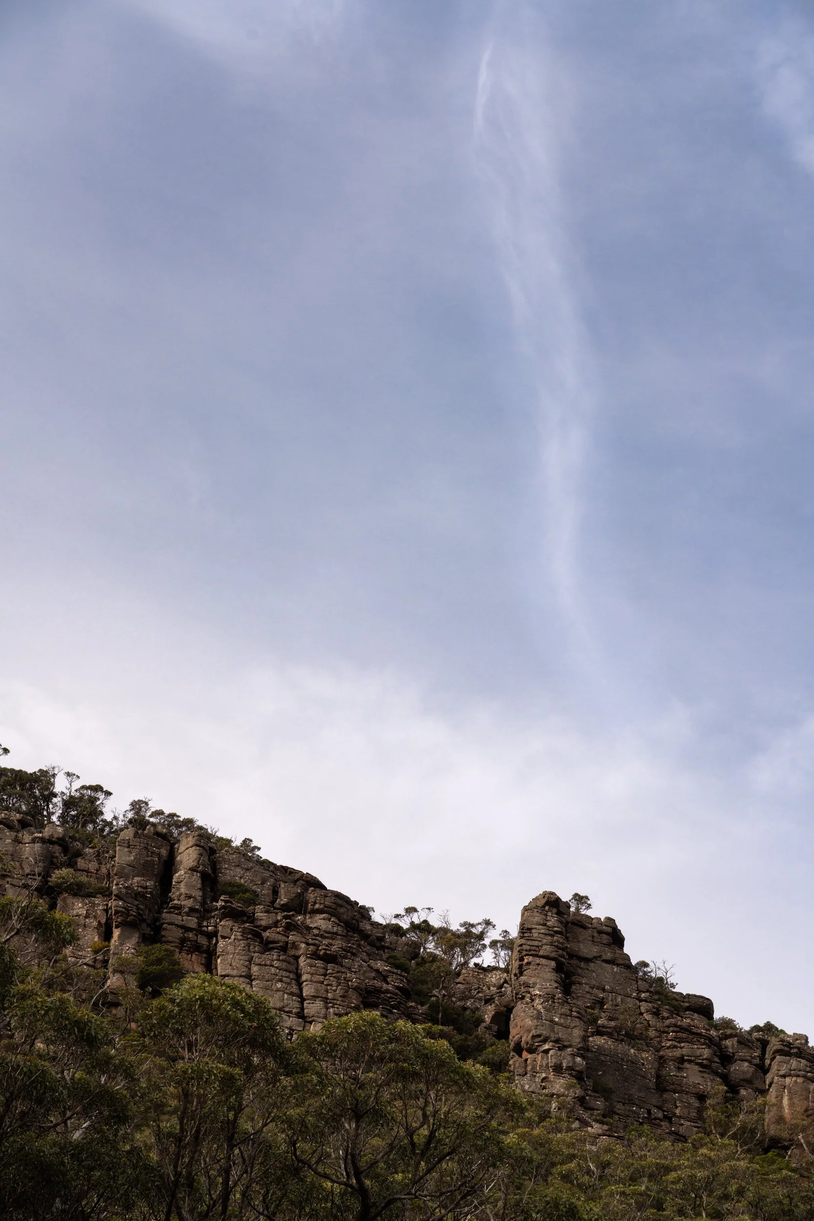 Cliffs with rocks and trees under a blue sky with wispy clouds.
