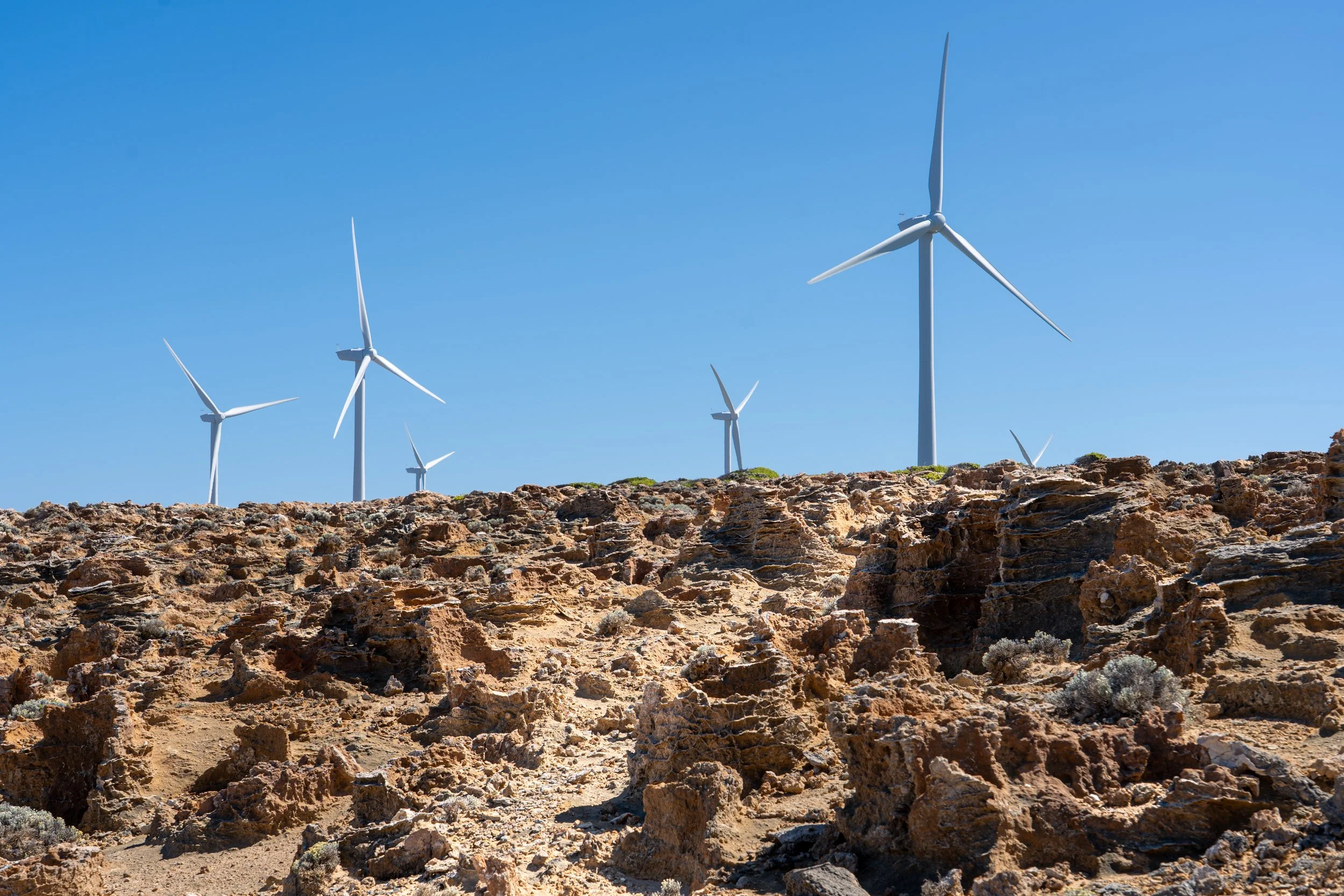 Multiple white wind turbines on rocky desert landscape under clear blue sky.