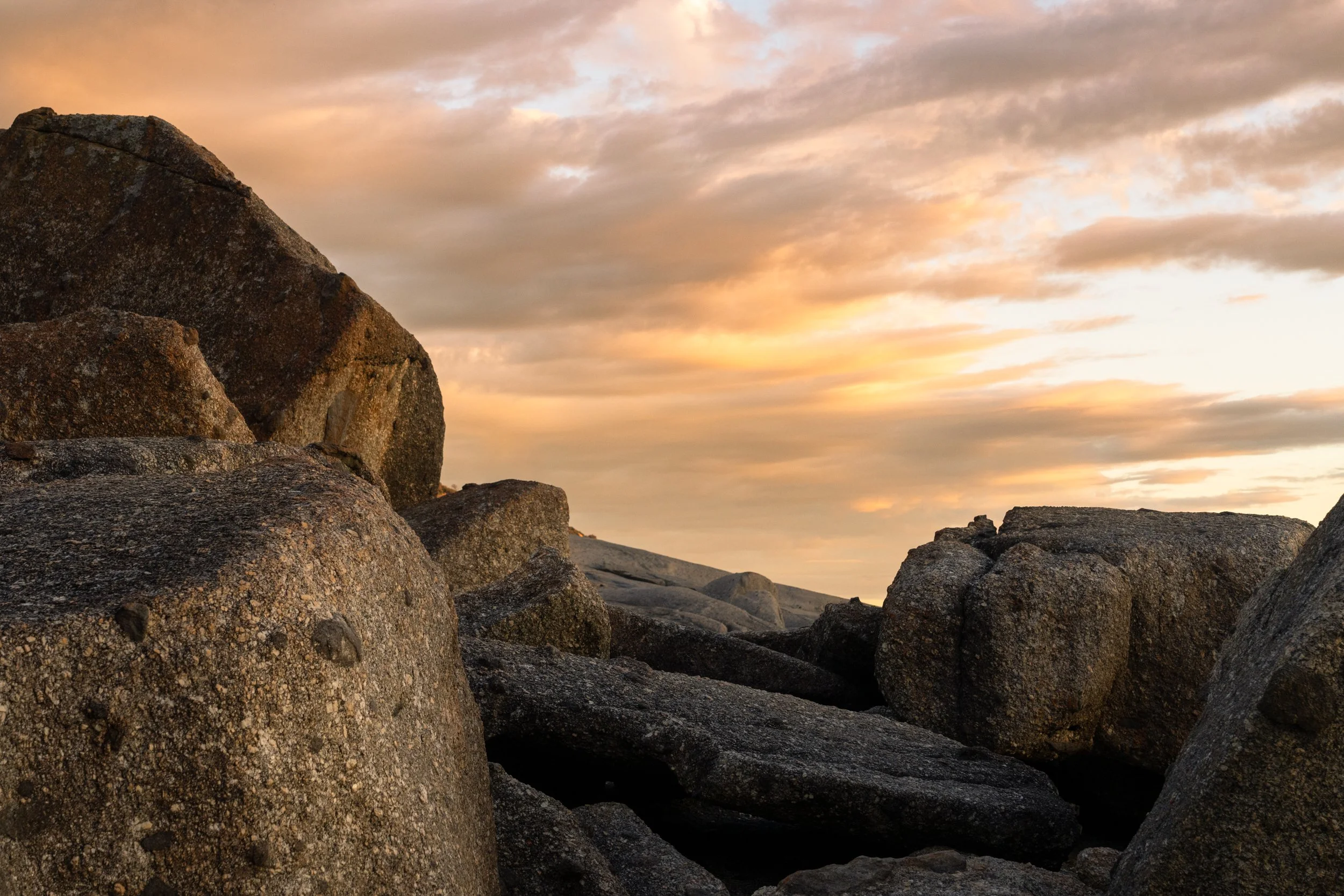Large rocks on a beach during sunset with a cloudy sky.