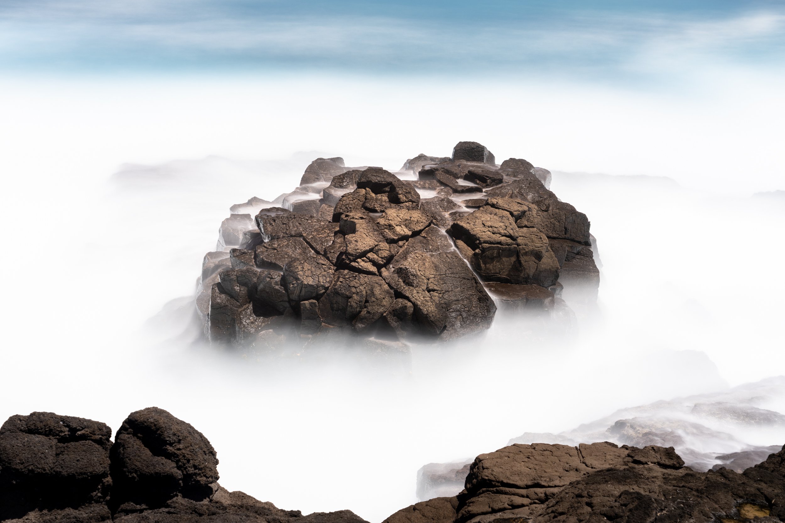 Rock formation surrounded by ocean waves with long exposure creating a misty effect