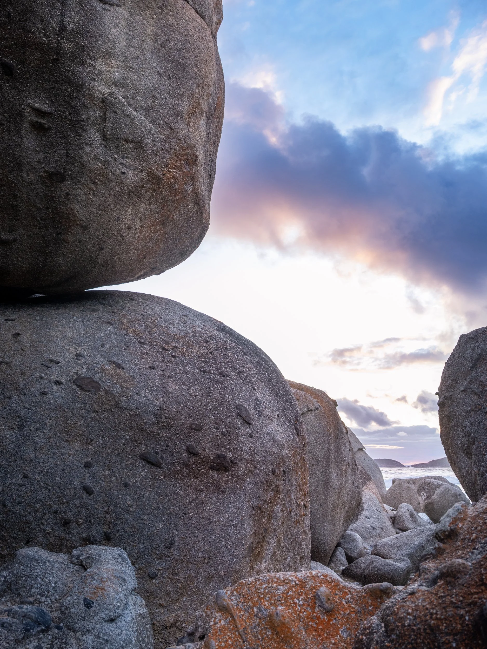 Large rocks and boulders on a beach with a cloudy sky at sunset