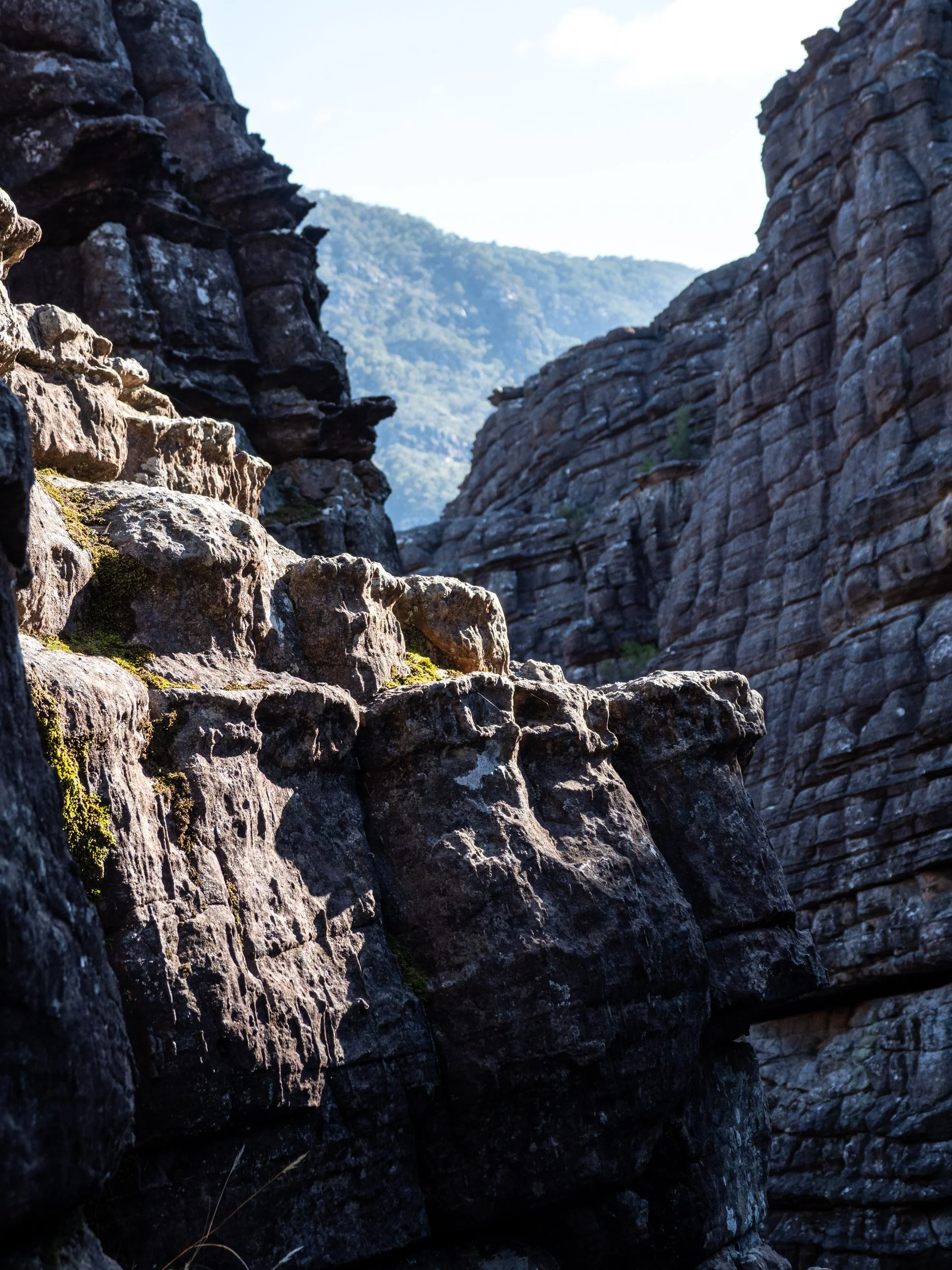 Rocky canyon with large weathered boulders and cliffs, distant mountain in the background under a clear sky.
