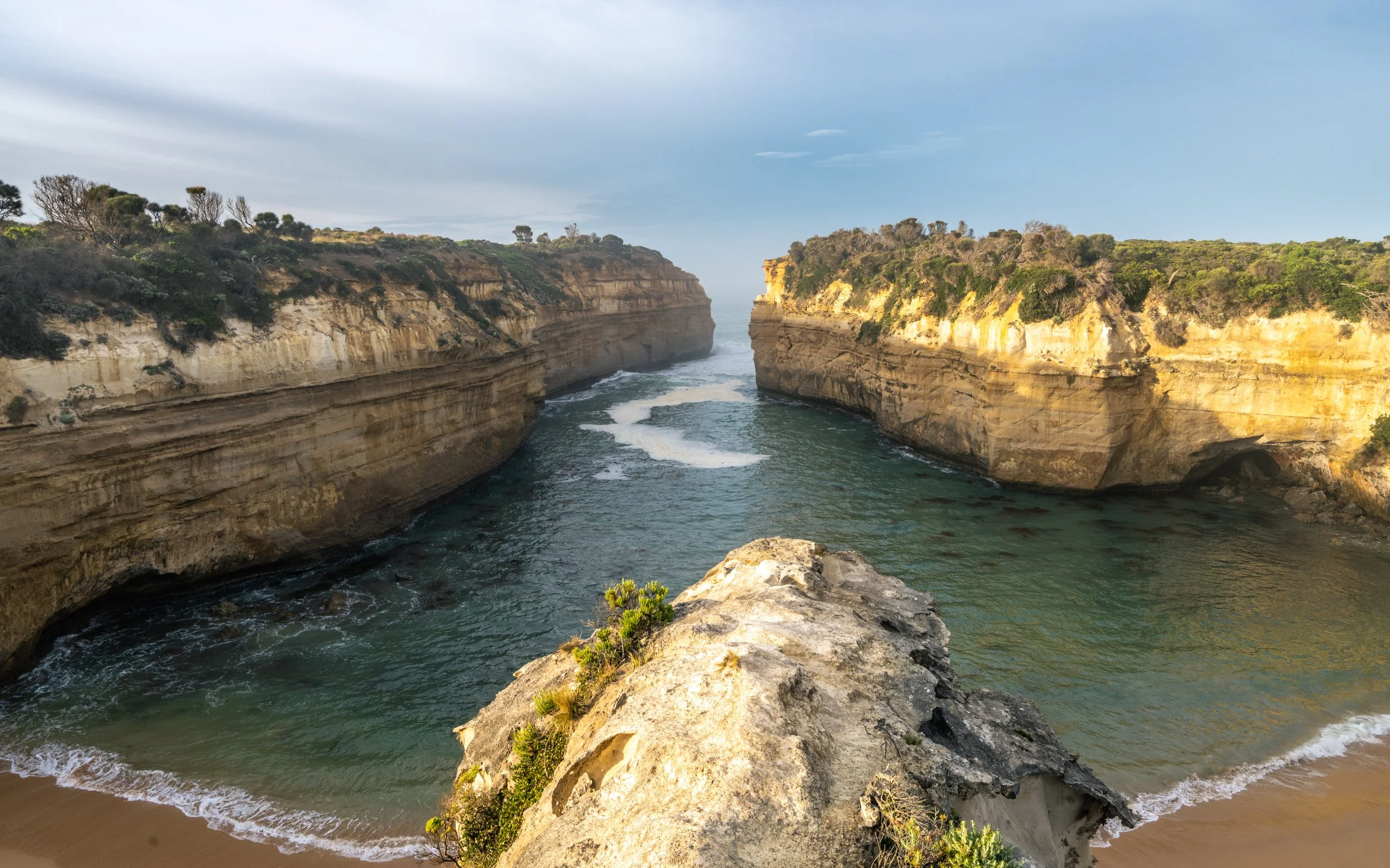 A scenic view of the rugged coastline with steep cliffs on both sides and a narrow waterway between them, with gentle waves and a partly cloudy sky.