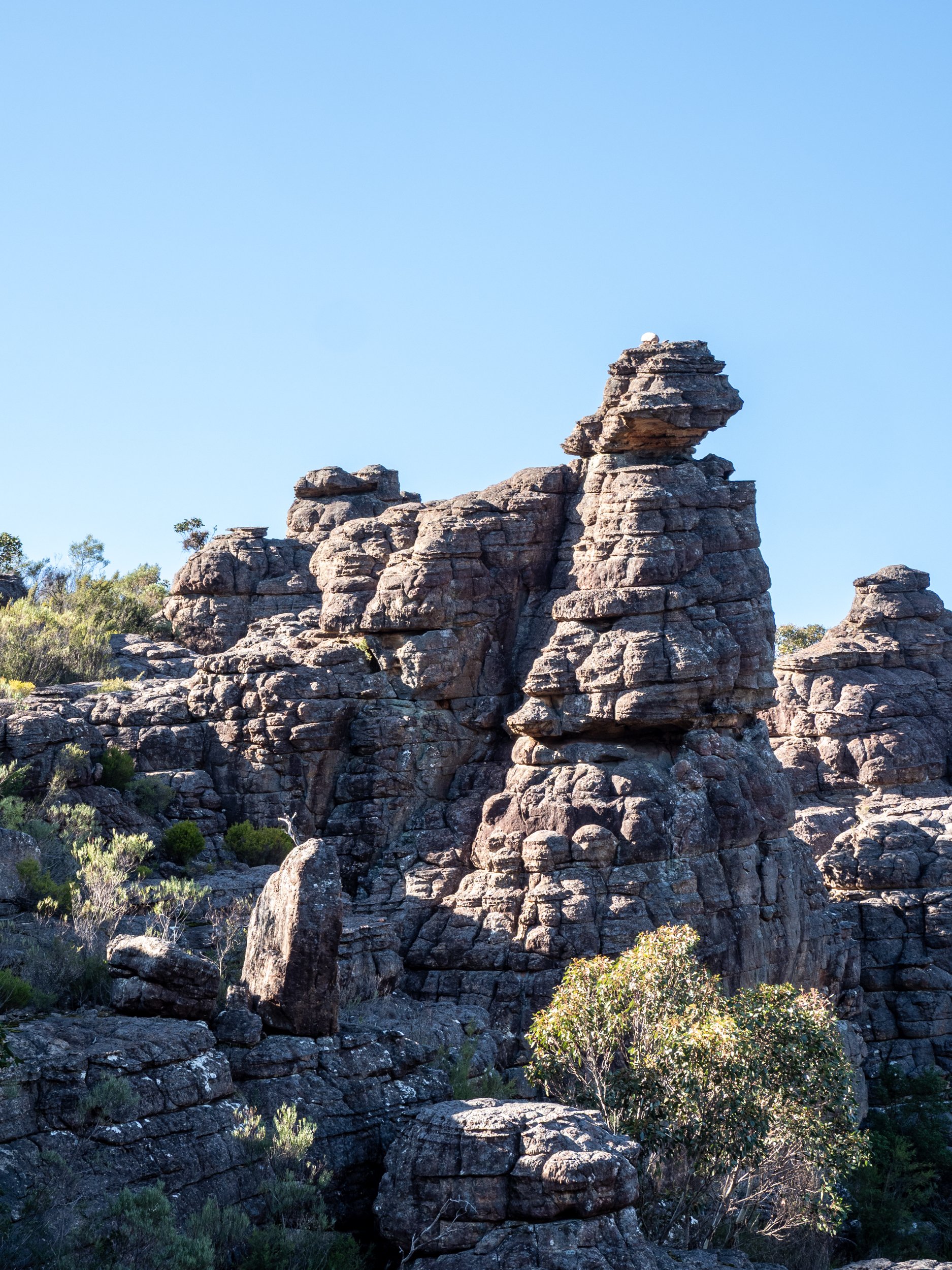 Rock formations with a clear blue sky and some greenery in the foreground.