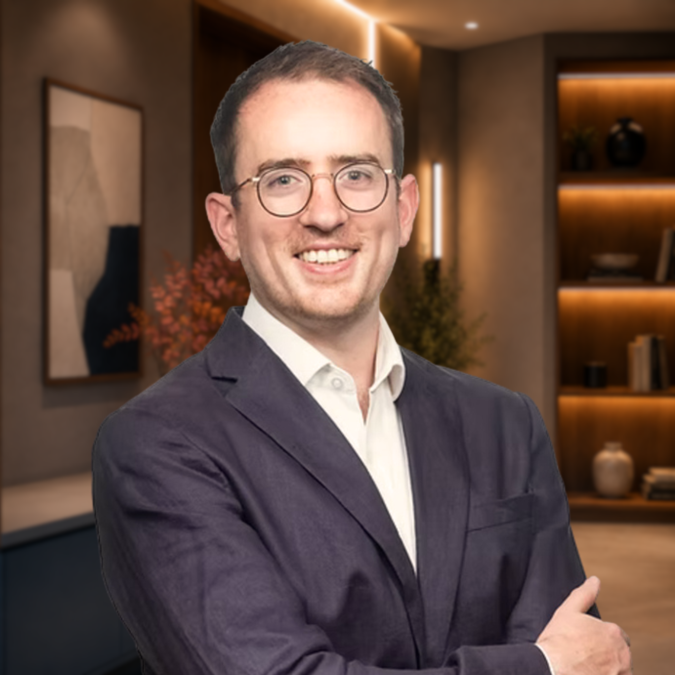 A young man with glasses wearing a dark blazer and white shirt, smiling with arms crossed, against a white background.