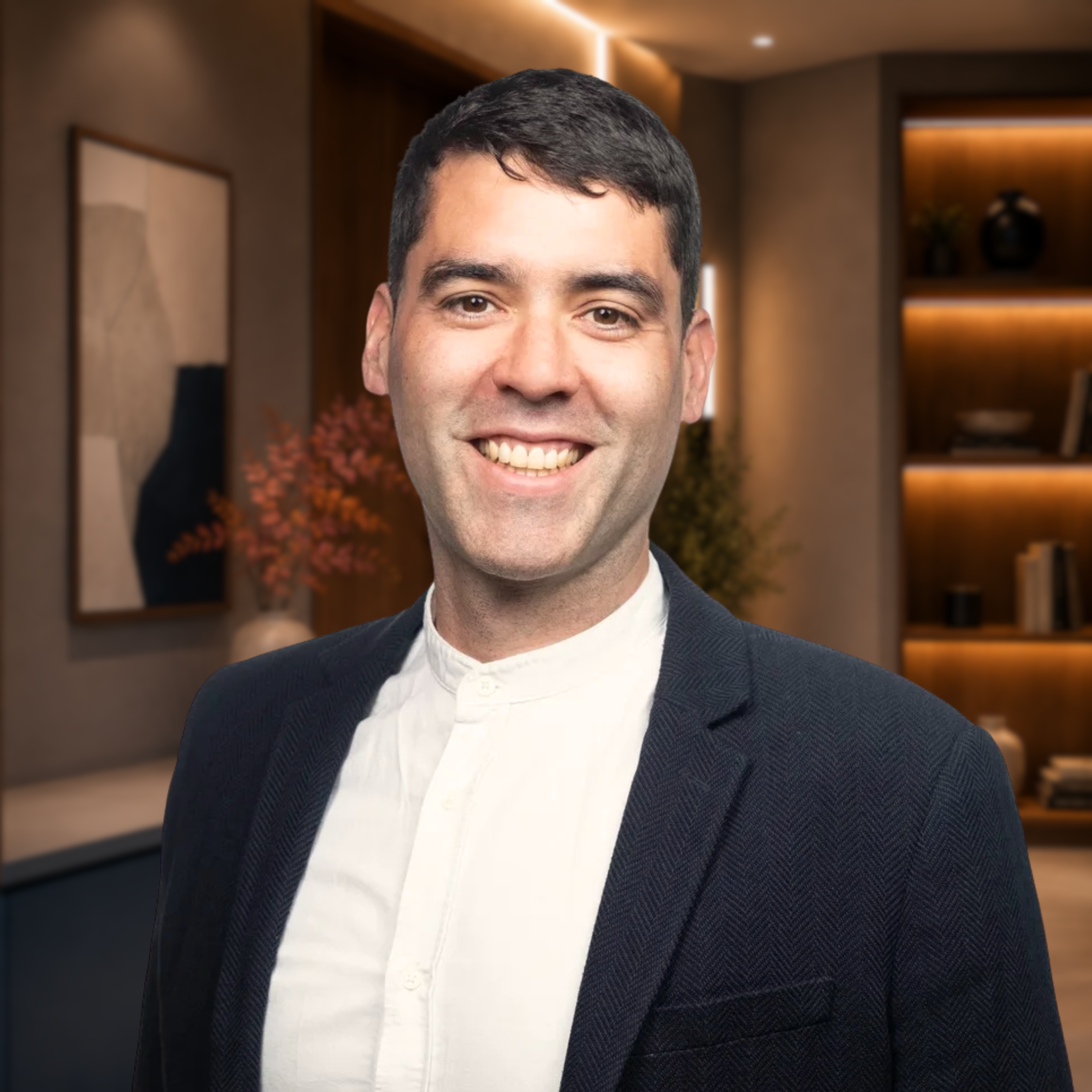 A smiling man in a dark blazer and white shirt against a plain white background.
