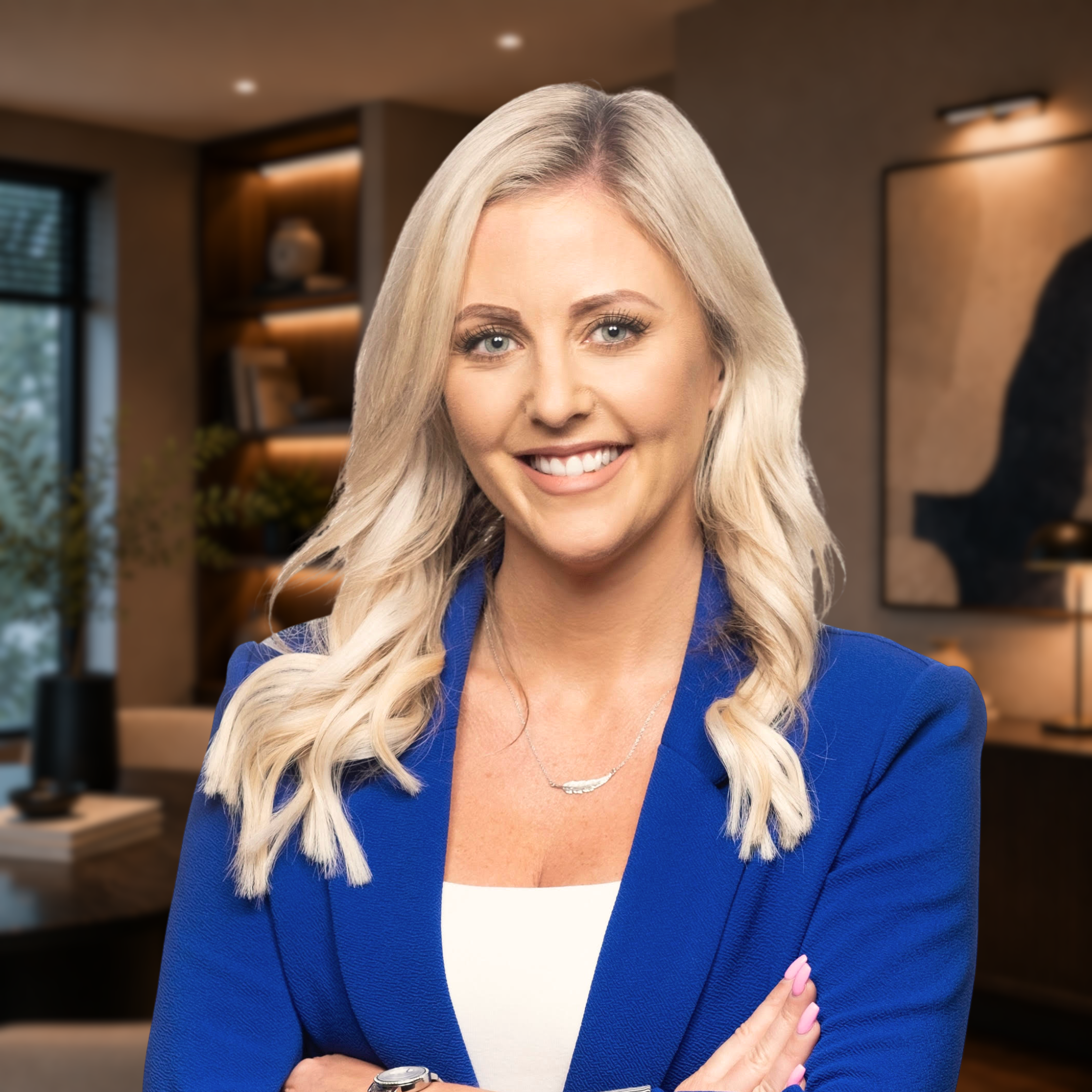 A blonde woman wearing a blue blazer and white top, smiling with arms crossed against a white background.