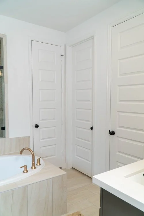 A bathroom with three white paneled doors, a bathtub with a gold faucet, and a white countertop.