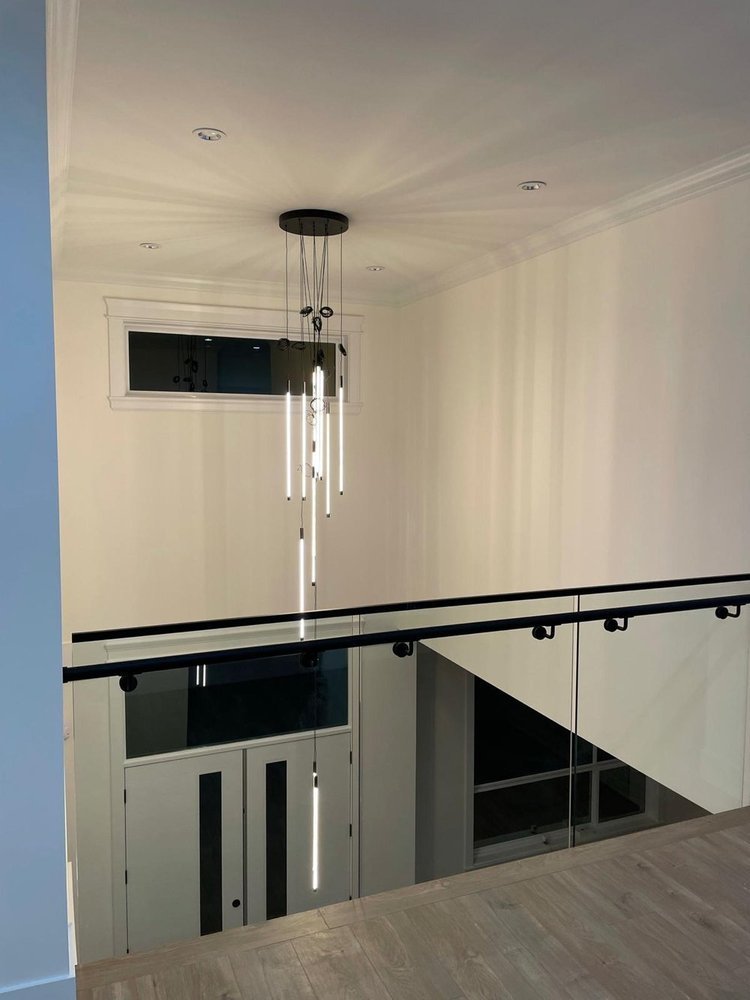 Modern interior with a staircase, glass railing, white walls, and a contemporary chandelier hanging from a white ceiling.