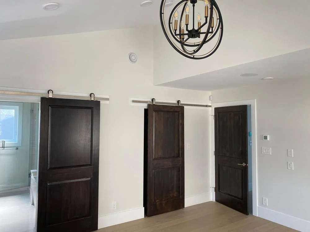 Interior room with white walls, dark sliding barn doors, a dark traditional door, hardwood floor, and a black metal chandelier with multiple exposed bulbs.