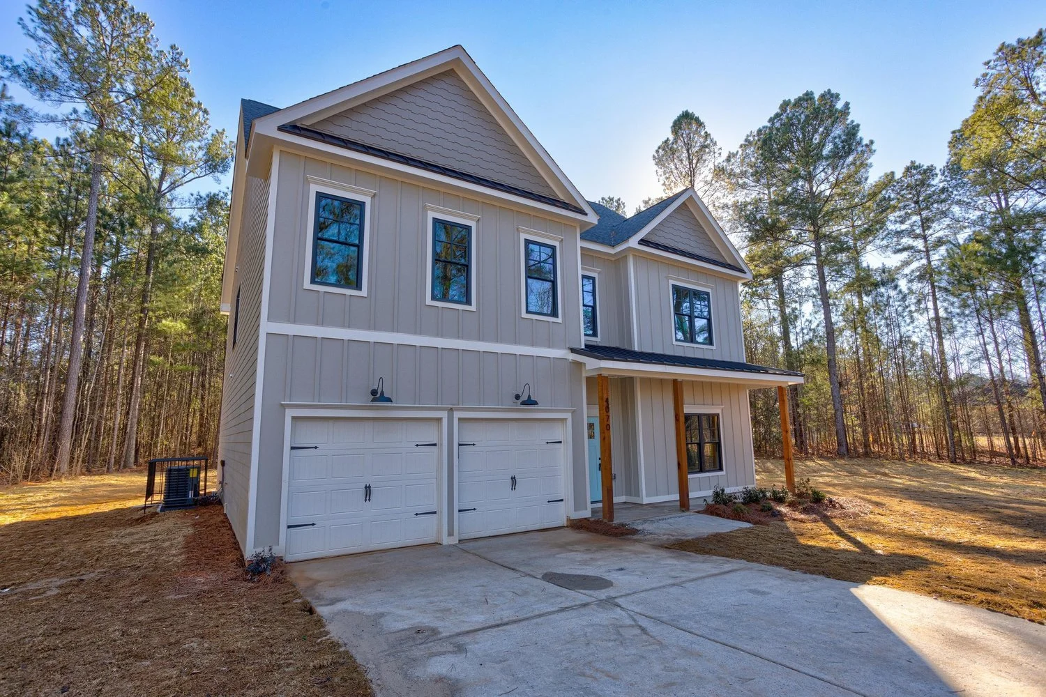 New two-story house with a gray exterior, black window frames, and a double garage, surrounded by trees on a clear day.