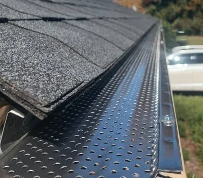 Close-up of a metallic gutter with a perforated cover on a roof with asphalt shingles, outside in daylight