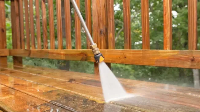 A pressure washer spraying water on a wooden deck.