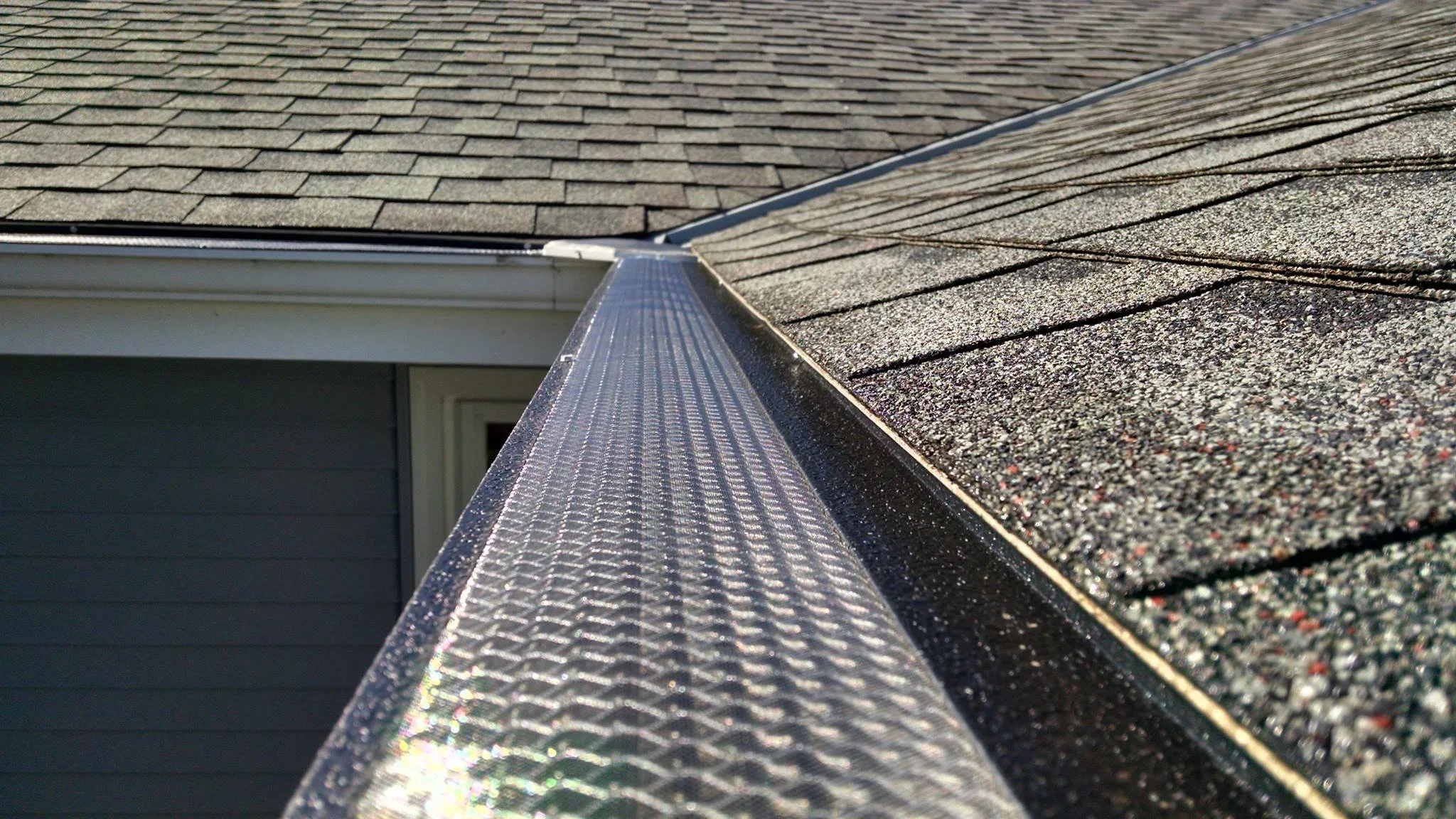 Close-up view of a house roof with asphalt shingles and a metal gutter.