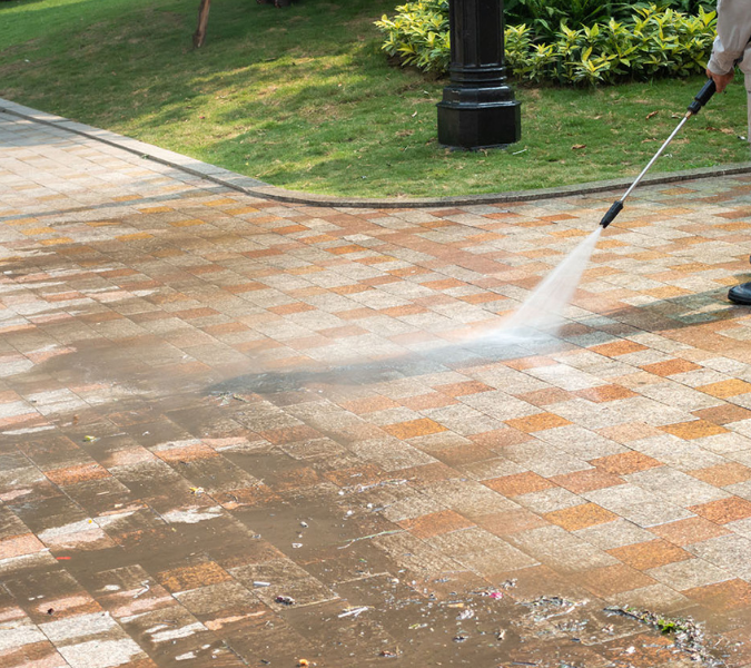 Person pressure washing a brick sidewalk outdoors