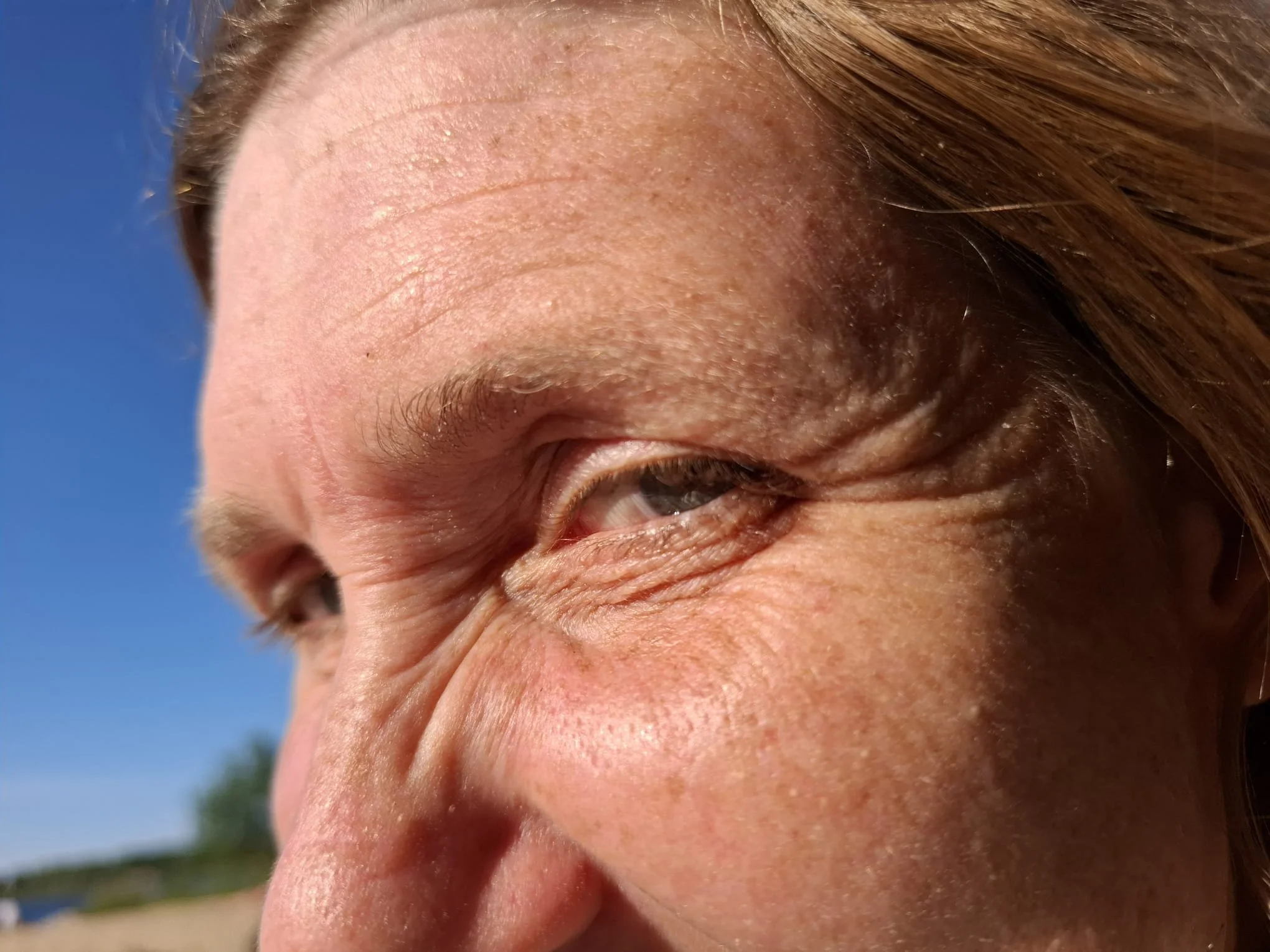 Nahaufnahme eines lachenden Frau mit blonden Haaren, die in der Sonne lächelt, mit einer blauen Himmel im Hintergrund.