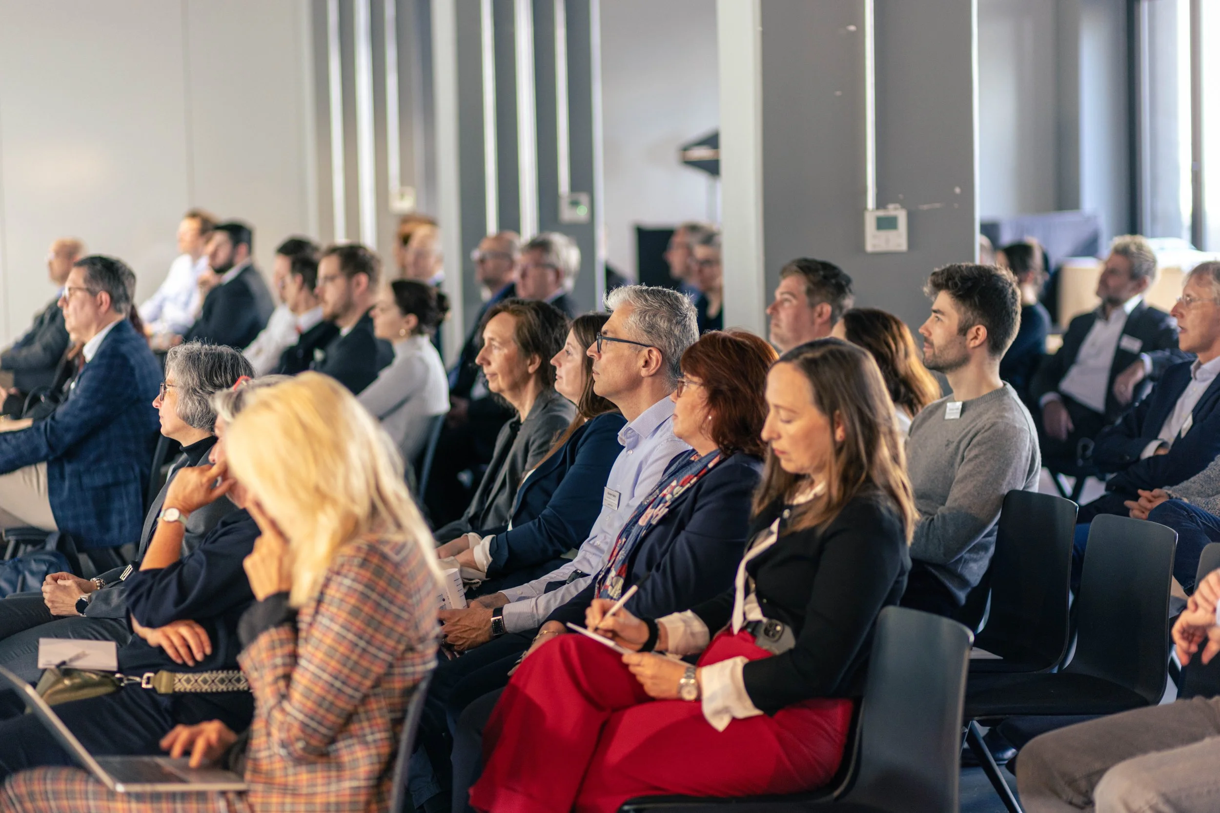 Menschen sitzen in einem Konferenzraum und hören aufmerksam einem Vortrag oder einer Präsentation zu.