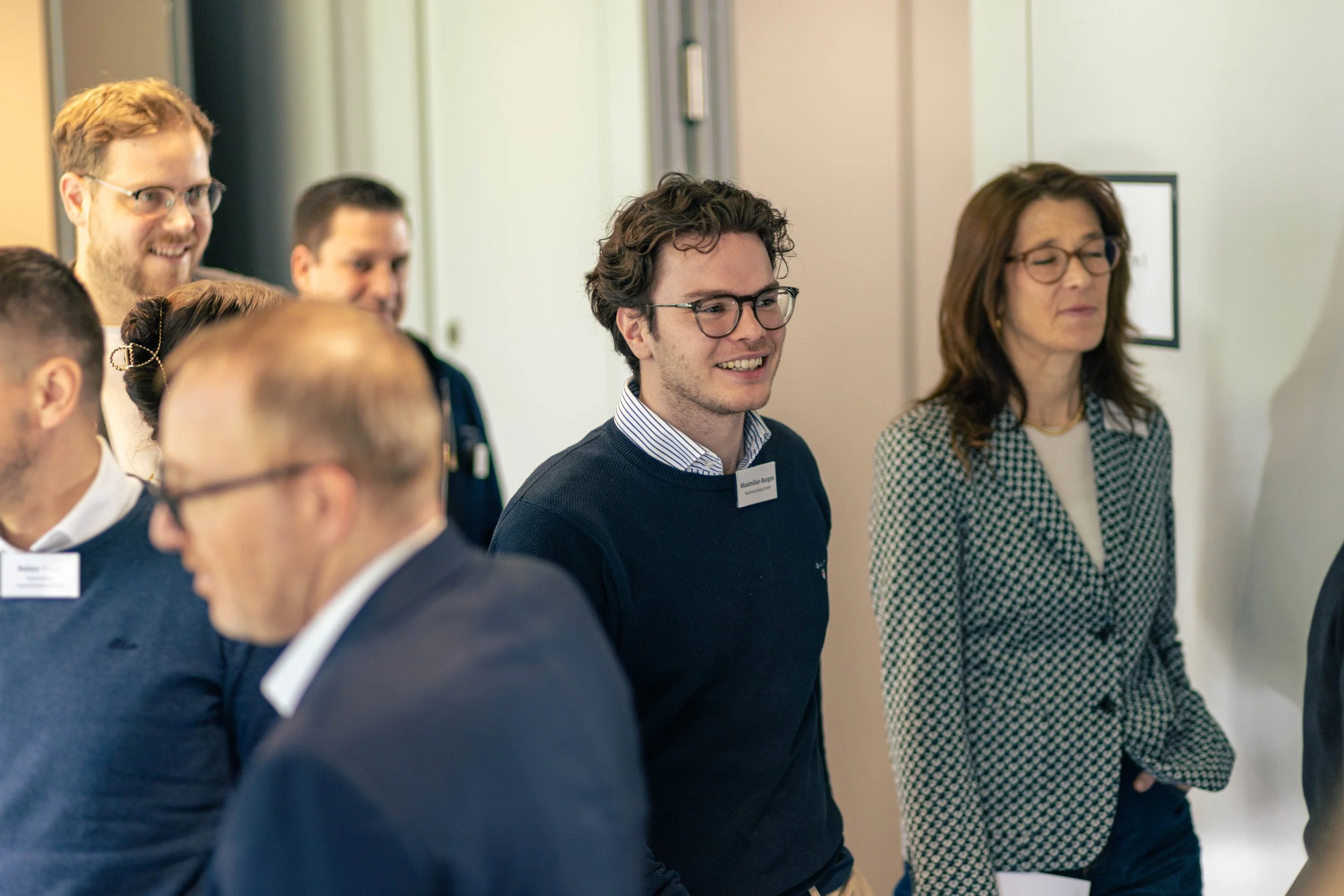 Menschen bei einer Veranstaltung, die sich in einer Reihe aufstellen, einige lachen, andere schauen ernst, in einem eleganten Umfeld.