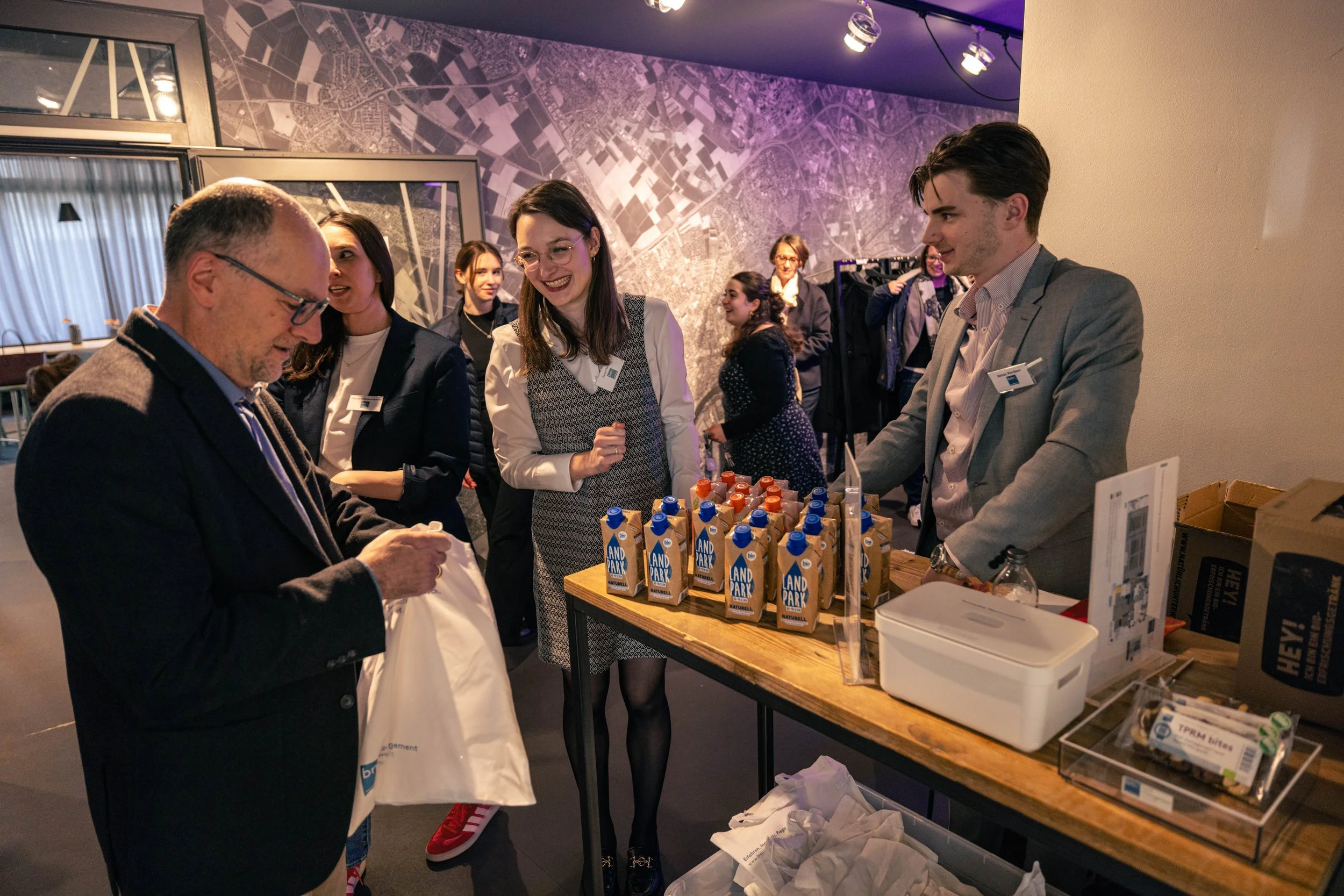 Menschen bei einem Event, die Getränke kaufen, Getränke in Tetra Pak Verpackungen auf einem Tisch, Verkäufer im Anzug, ein Mann mit Brille erhält eine Tüte.