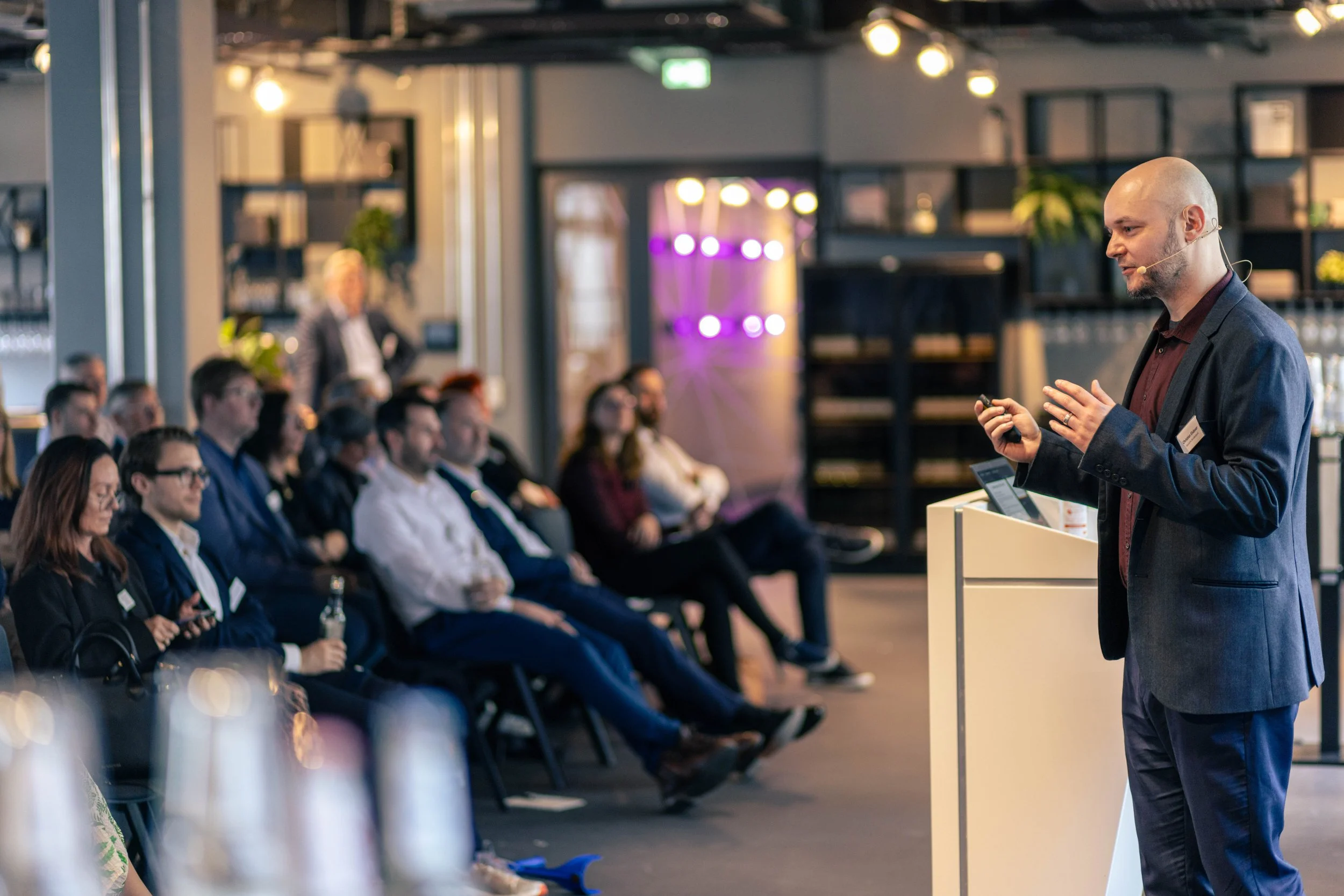 Mann hält Vortrag vor sitzender Gruppe bei Konferenz in moderner Location.