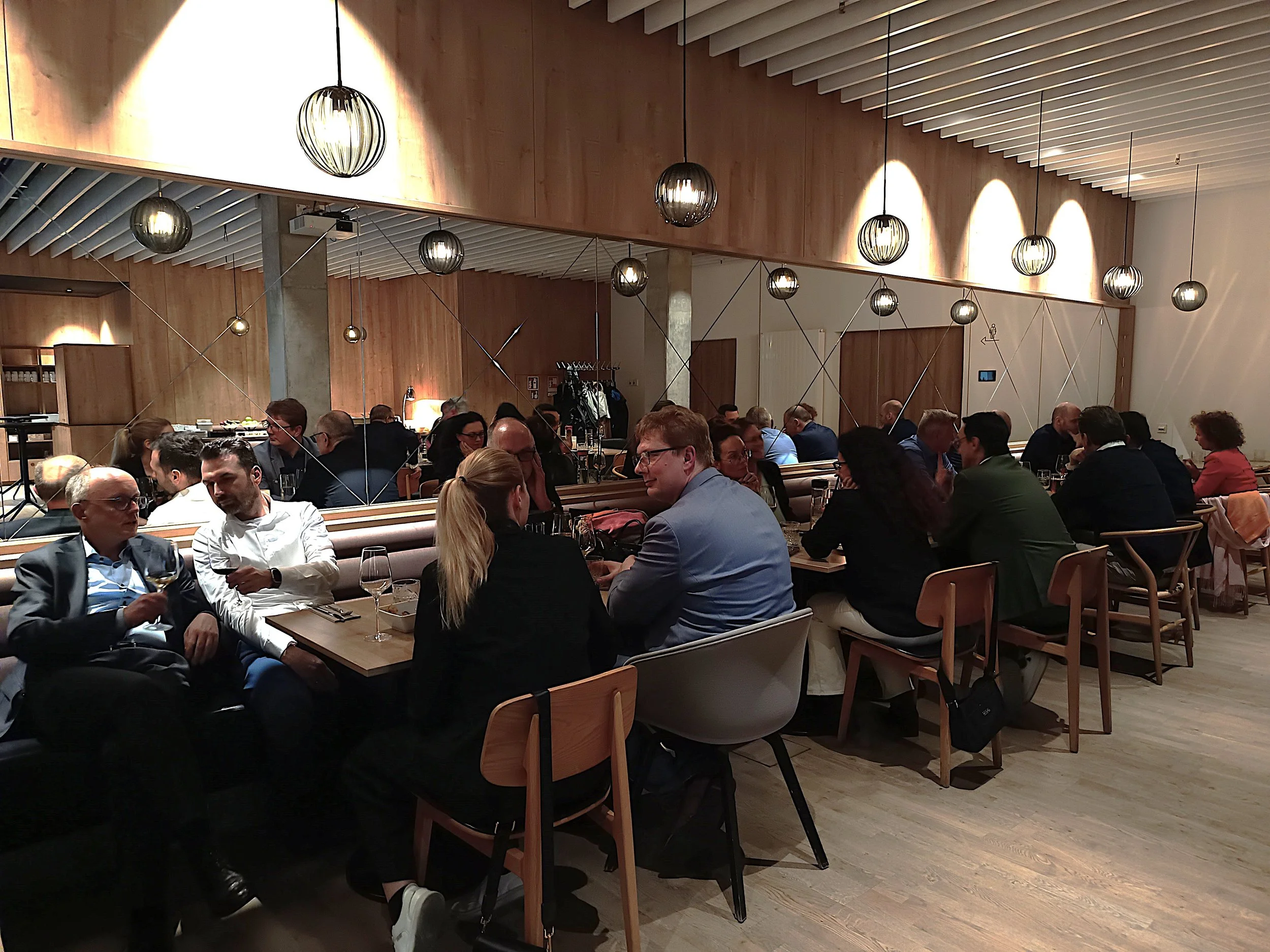 Menschen sitzen in einem modernen Restaurant oder einer Lounge, gesprochen in einer ruhigen und geselligen Atmosphäre, mit Holzinterieur und stilvoller Beleuchtung.