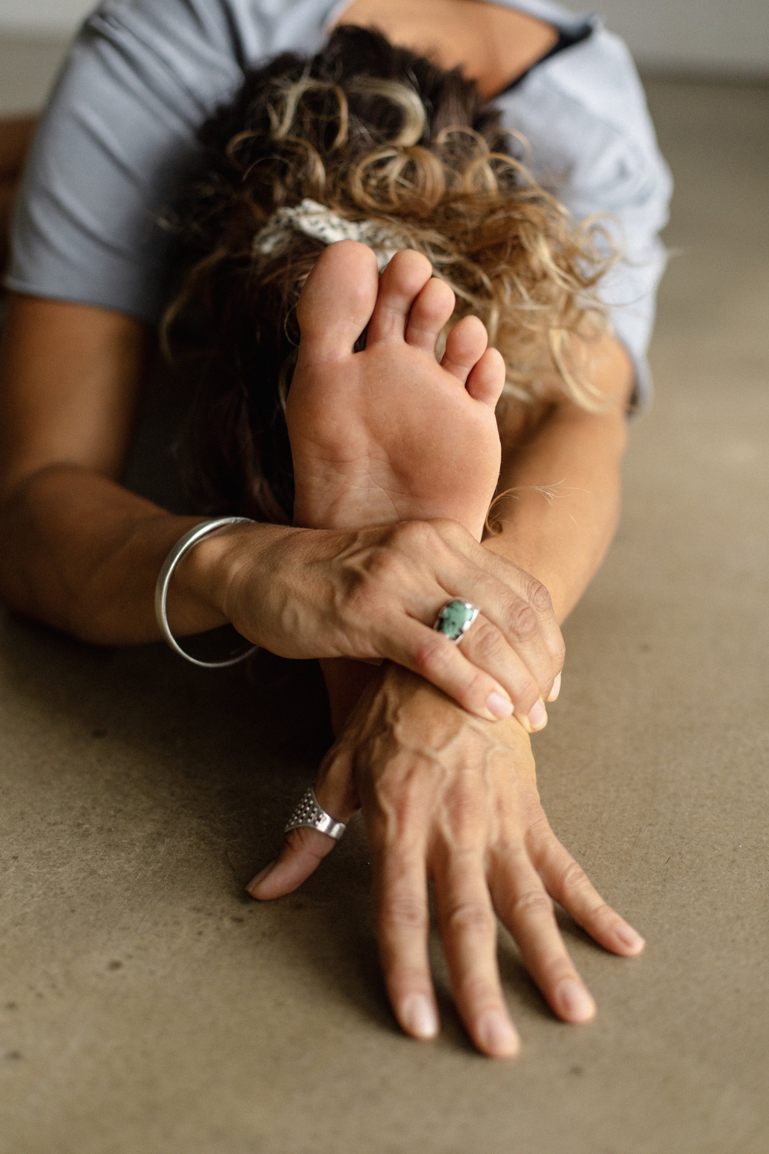 A woman is performing a yoga stretch on the floor, supporting herself with one hand and the foot of her raised leg, with the foot close to her face.