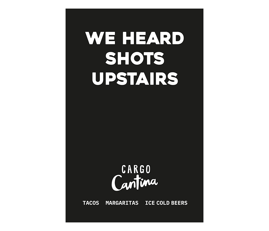 Signboard with a black background and white text indicating upstairs shots are available at Cargo Cantina, including tacos, margaritas, and ice cold beers.