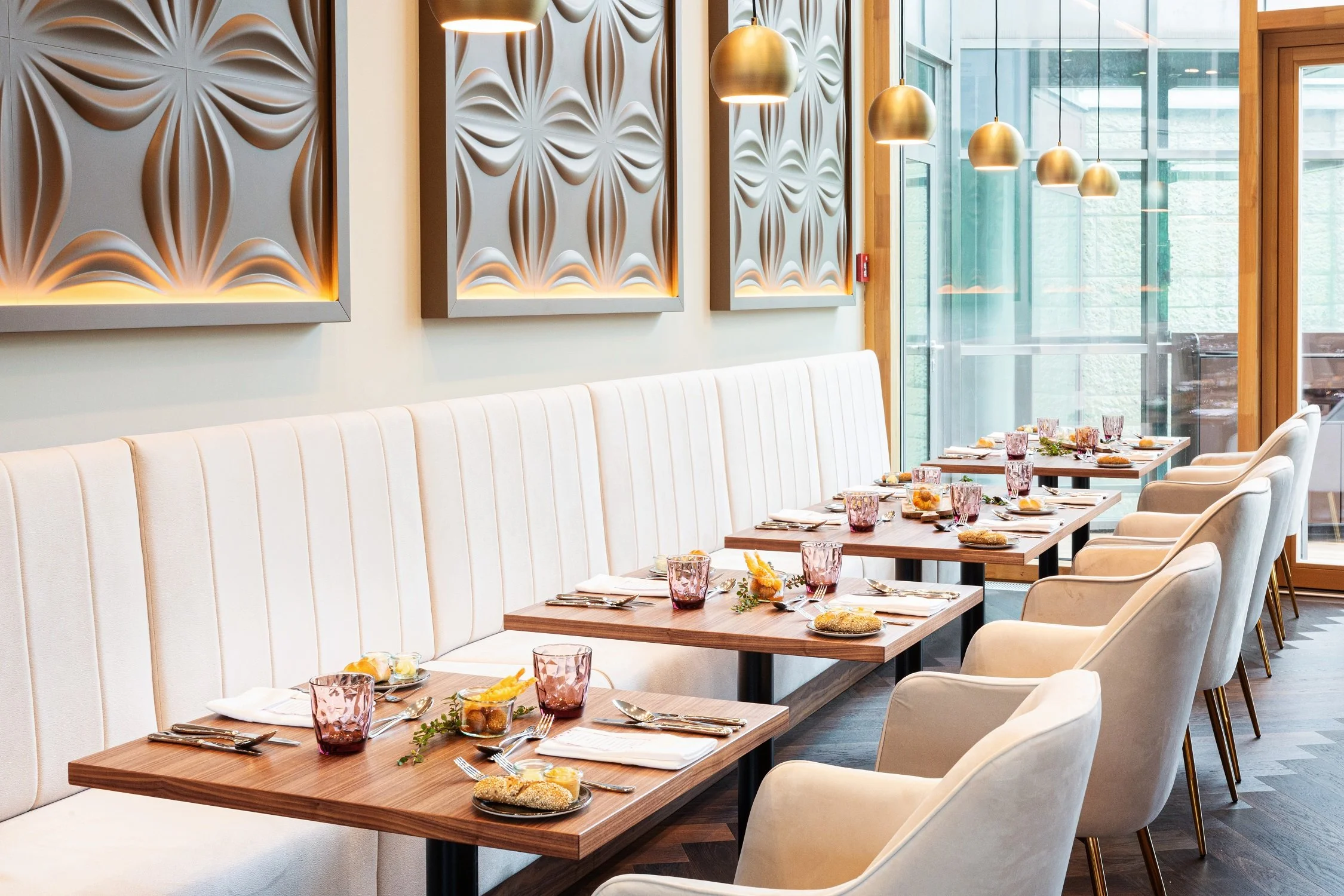 Modernes Restaurantinterieur mit gepolsterter Sitzbank, gedeckten Holztischen und dekorativer Wand mit indirekter Beleuchtung