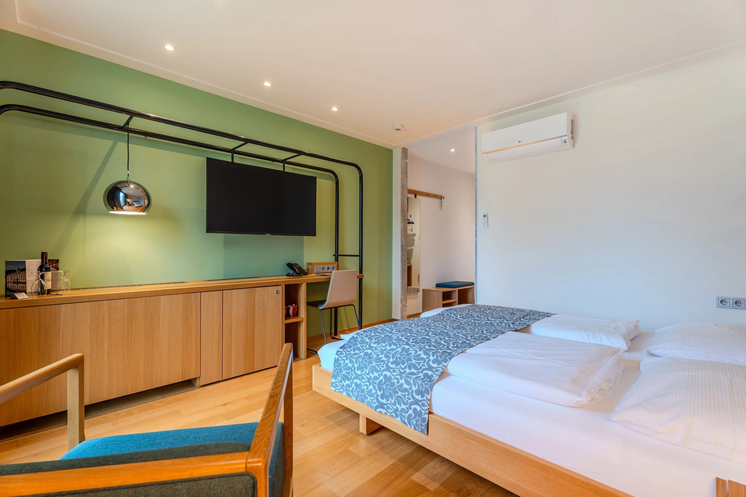 Modernes Hotelzimmer mit grünem Akzent, Bett, Schreibtisch und Wandfernseher.