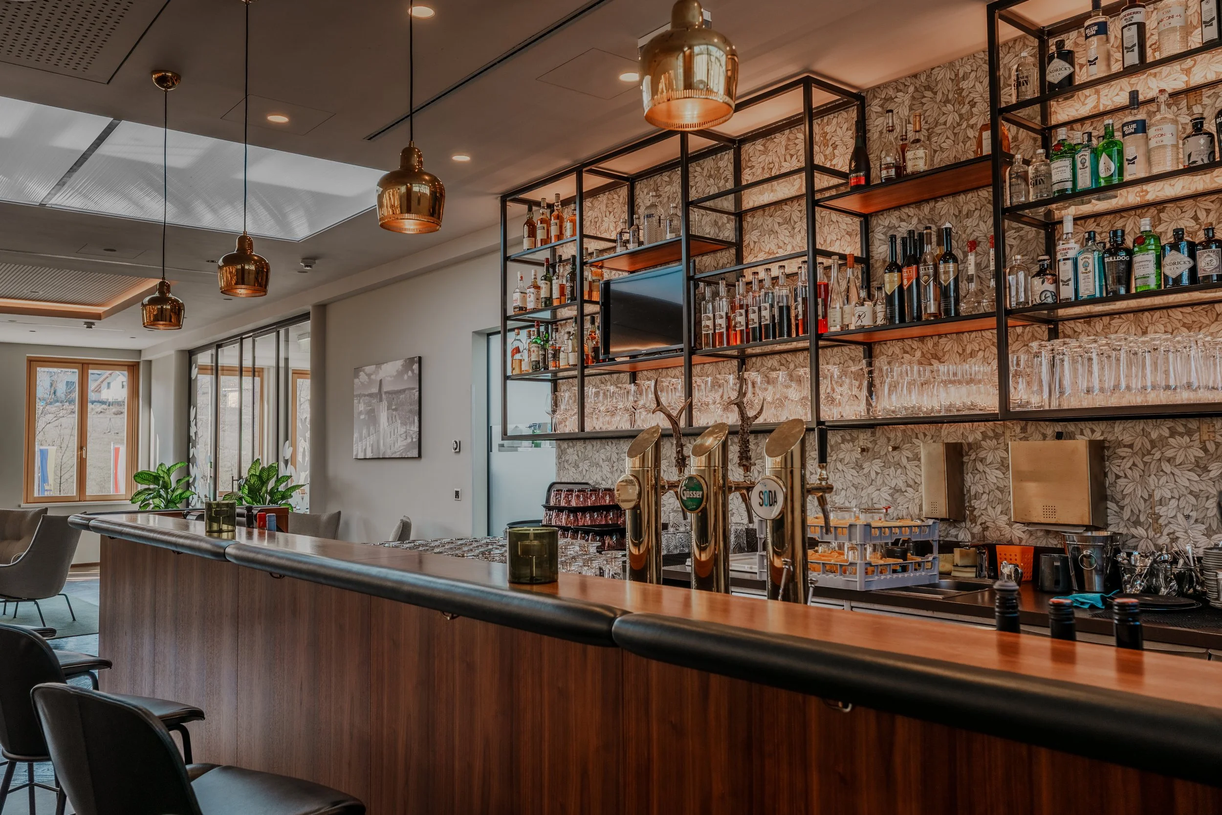Stilvolle Bar mit Holztheke, Zapfhähnen und dekorativen Regalen voller Spirituosen und Gläser im modernen Ambiente