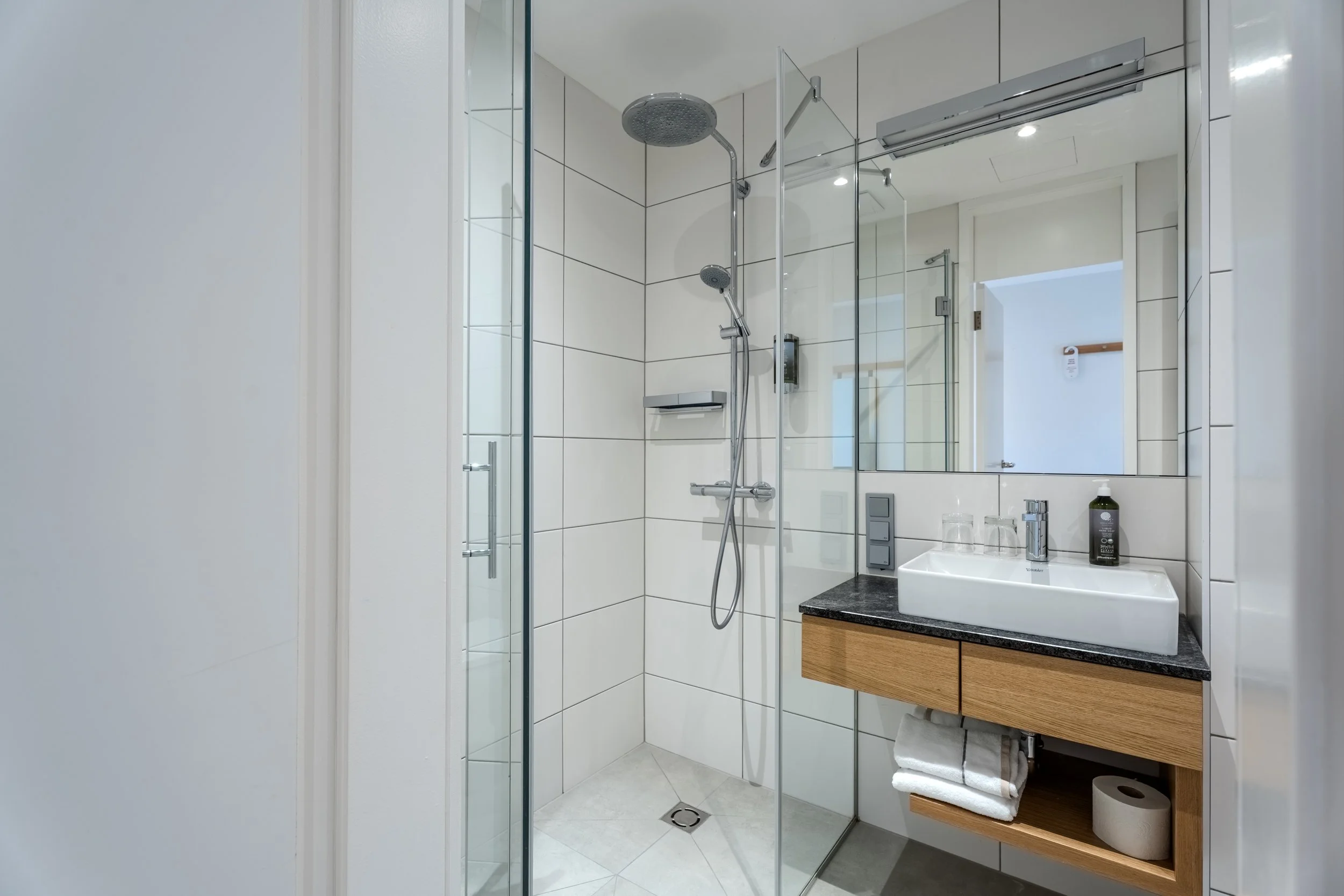 Helles Badezimmer mit Glasdusche, Waschbecken und Handtüchern in modernem Design.