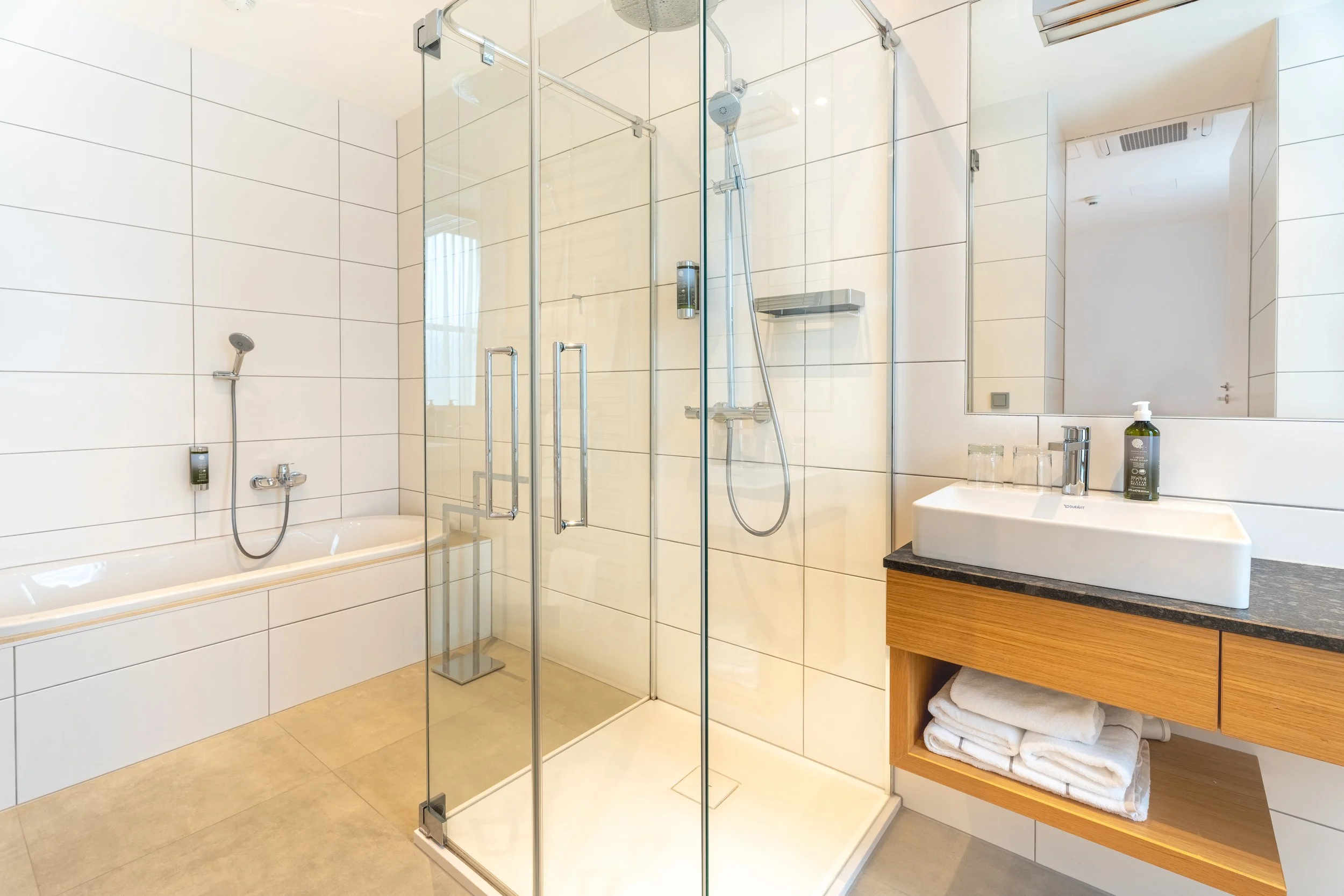 Modernes Badezimmer mit verglaster Dusche, Badewanne, Waschbecken und hellen Fliesen.