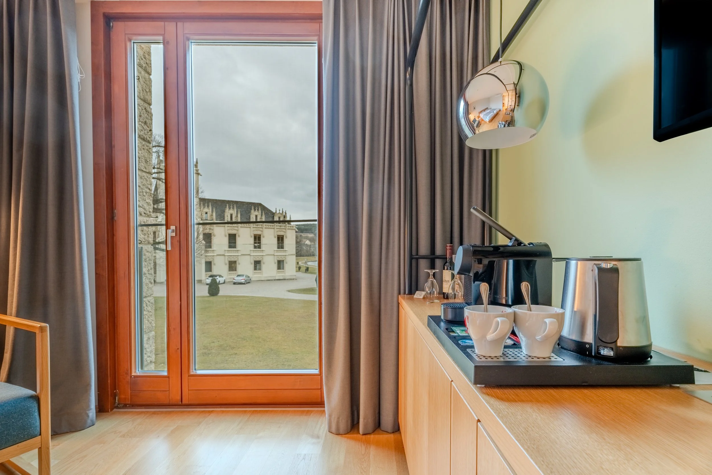 Hotelzimmer mit großem Fenster, Vorhängen und Blick auf ein historisches Gebäude im Freien.