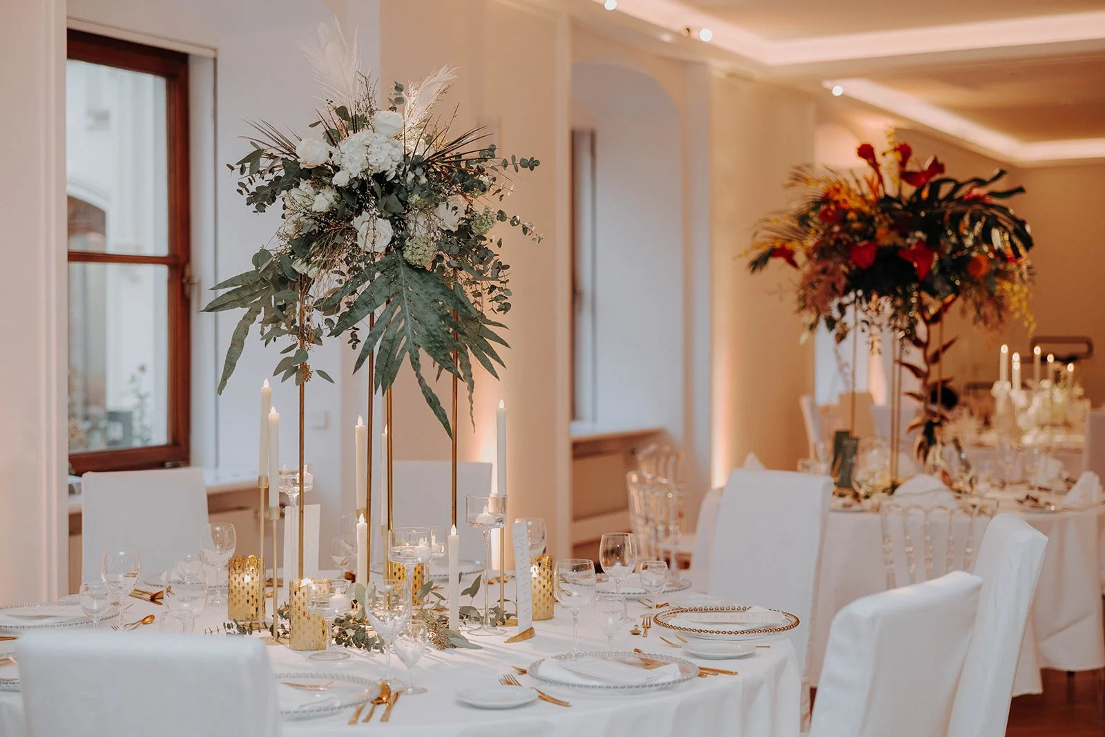 Elegante Hochzeitstischdekoration mit goldenen Kerzenhaltern und grünen sowie weißen Pflanzen als Tischdekoration