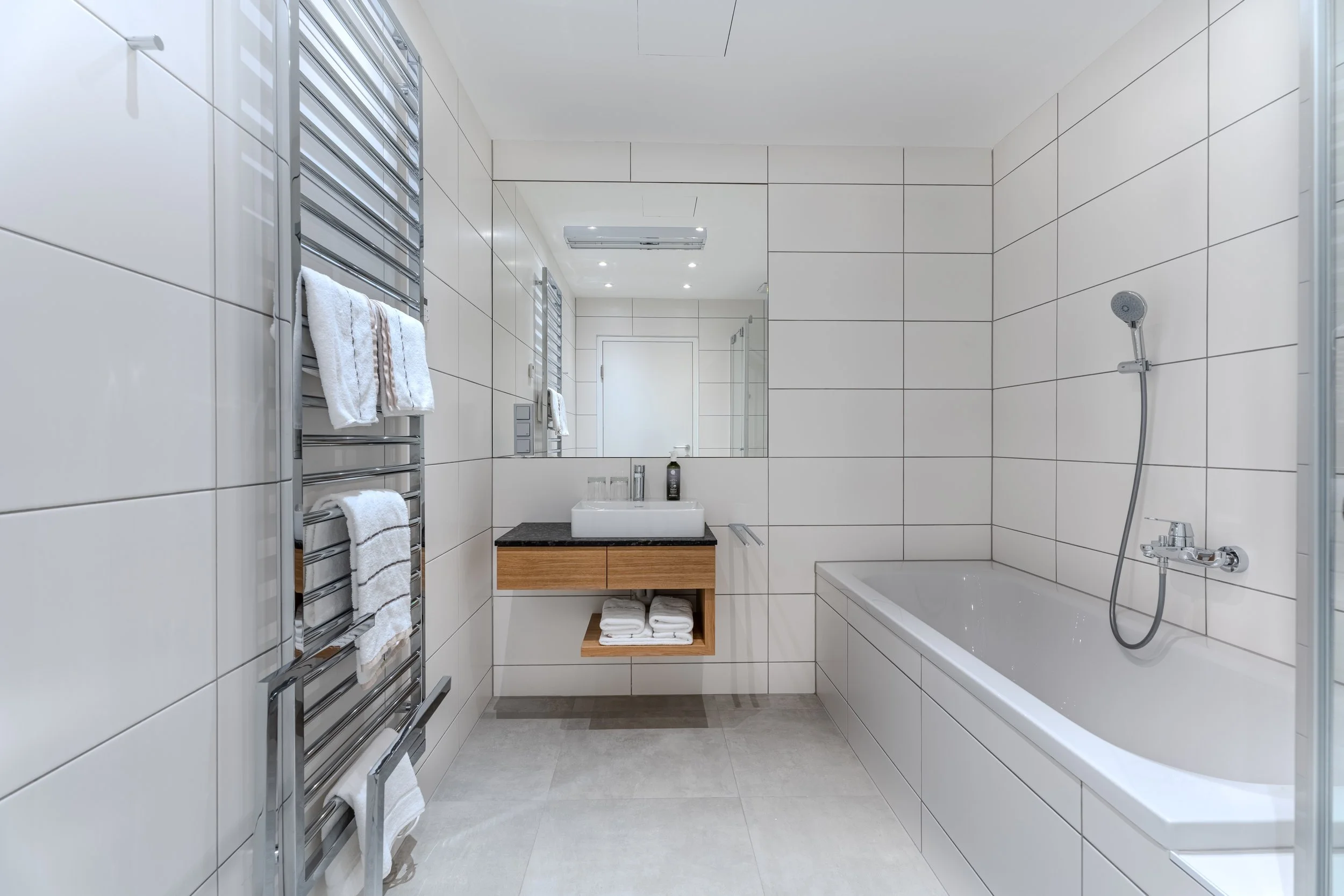 Modernes Badezimmer mit weiß gefliesten Wänden, Badewanne, Waschbecken und Handtuchheizkörper.