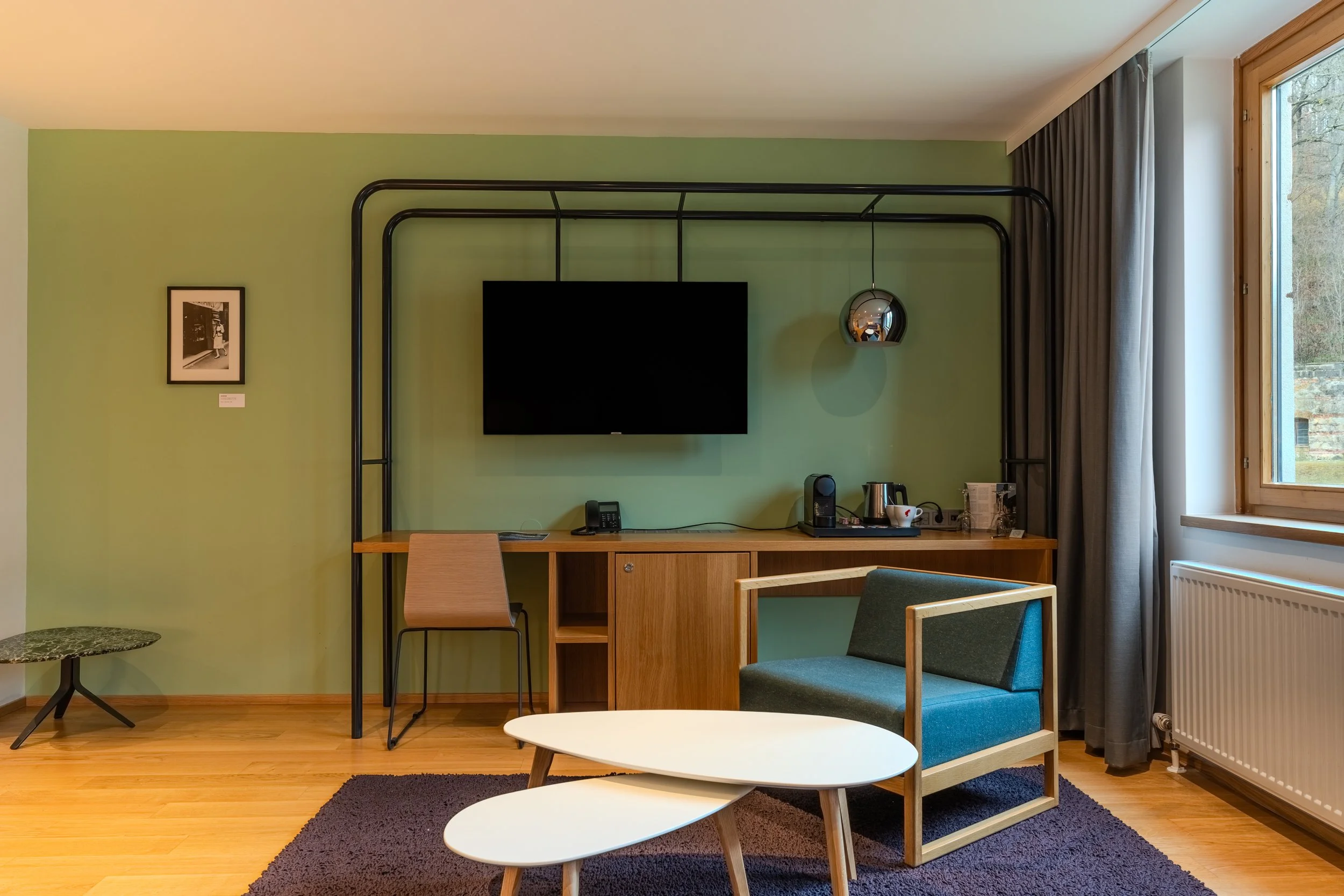 Modern eingerichteter Wohnbereich mit Schreibtisch, Stuhl, wandmontiertem Fernseher und grüner Akzentwand