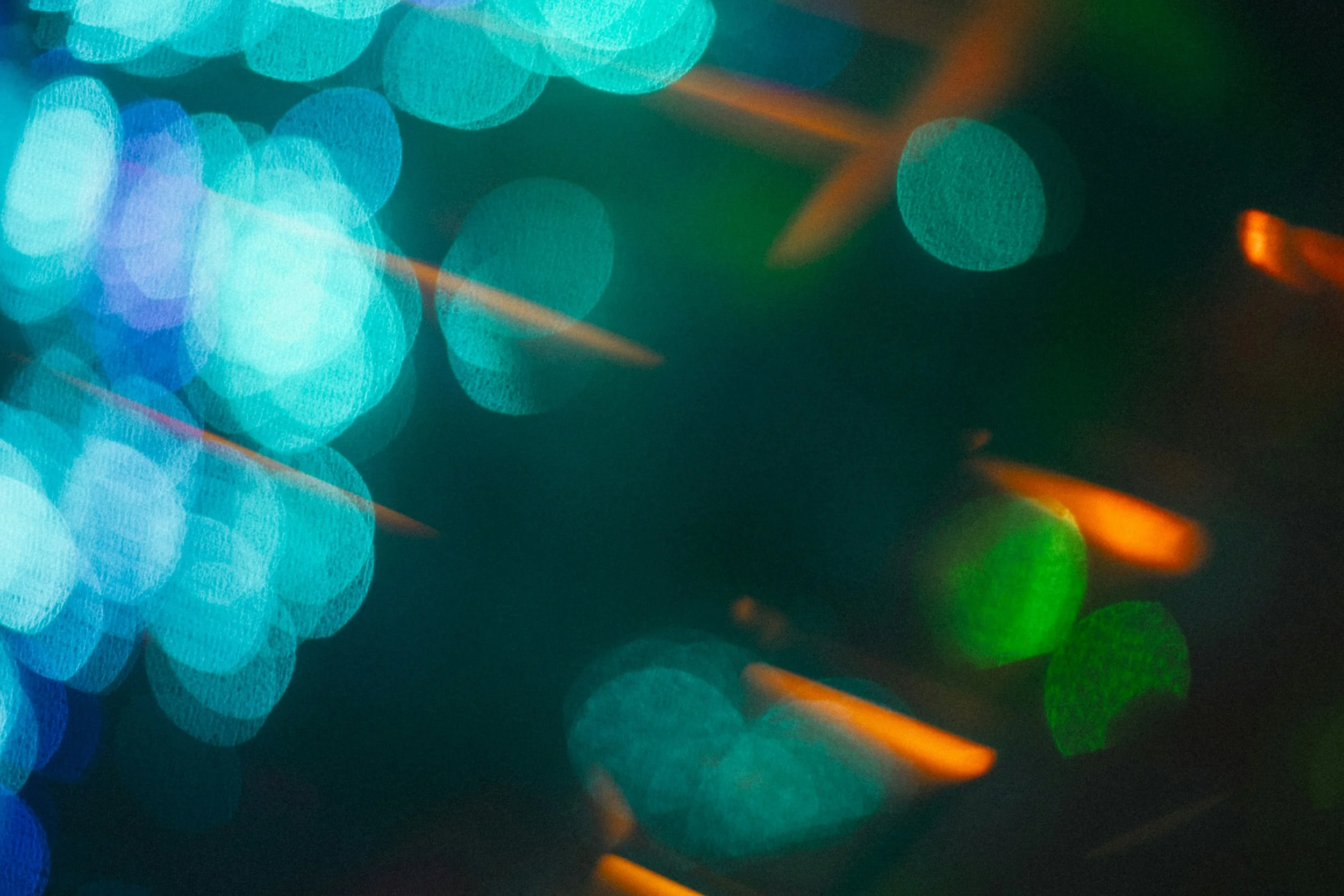 Abstract image of colorful bokeh lights with blue, green, and orange hues against a dark background.