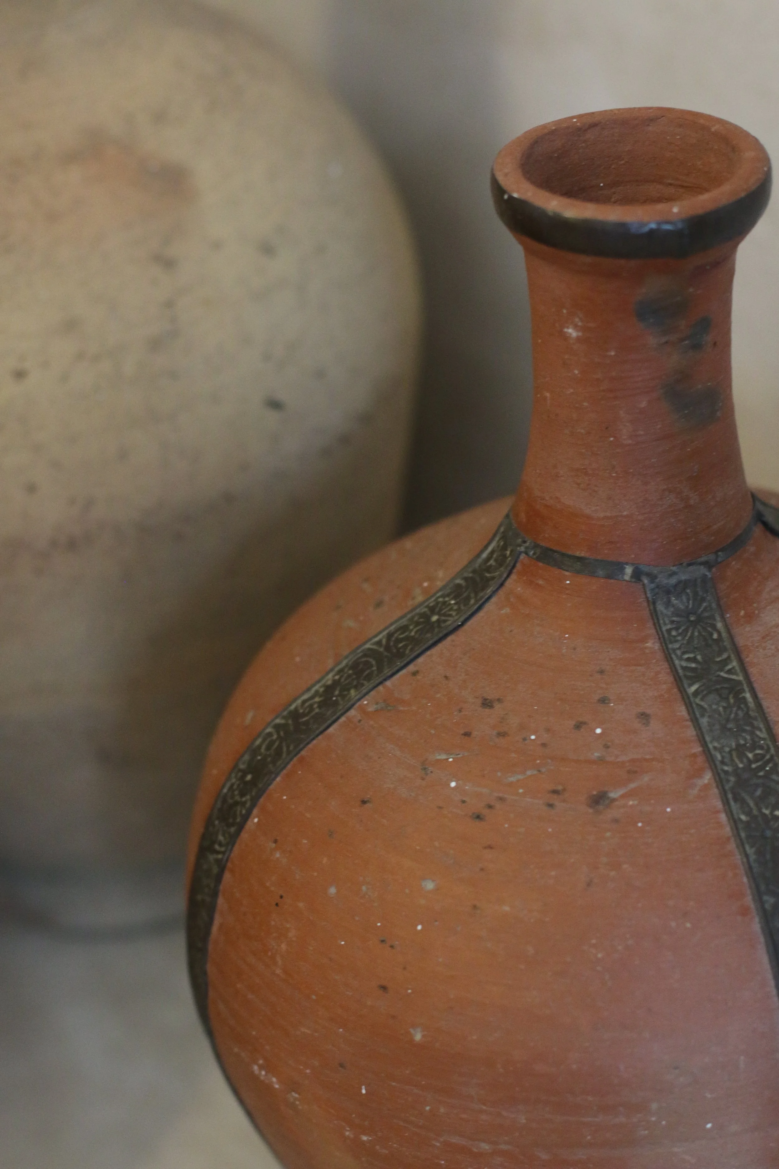 Une jarre en terre cuite avec des motifs en métal, placée à côté d'une autre jarre beige.