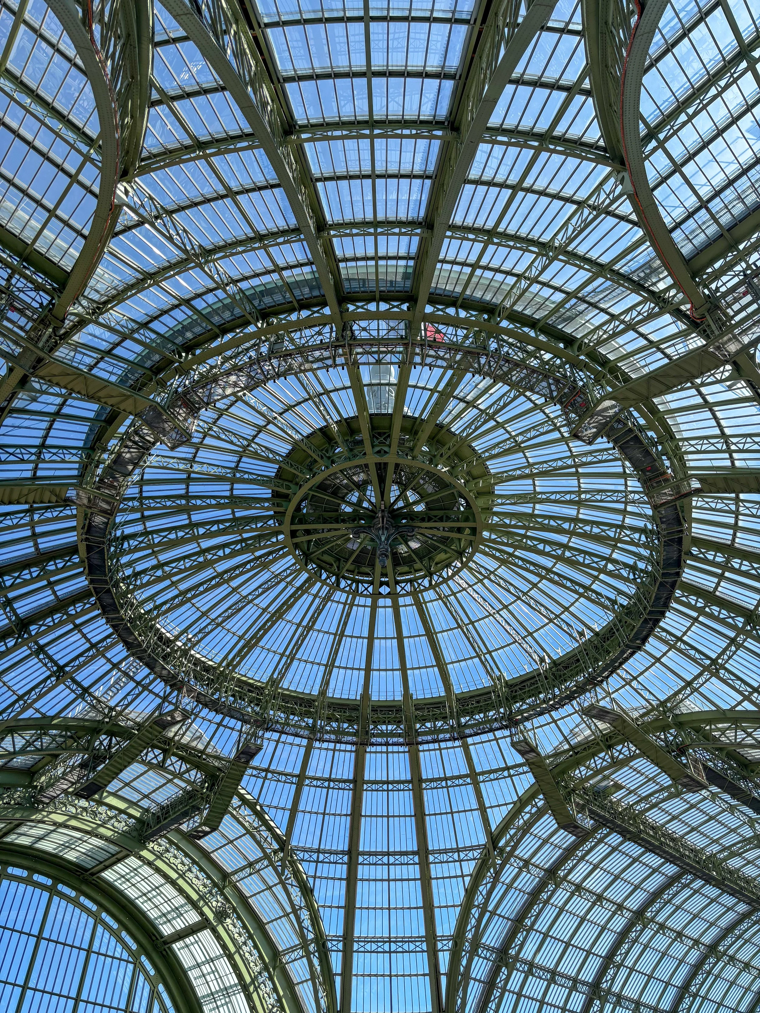 Vue du plafond en verre d'une structure métallique en spirale, avec le ciel bleu visible à travers le verre.