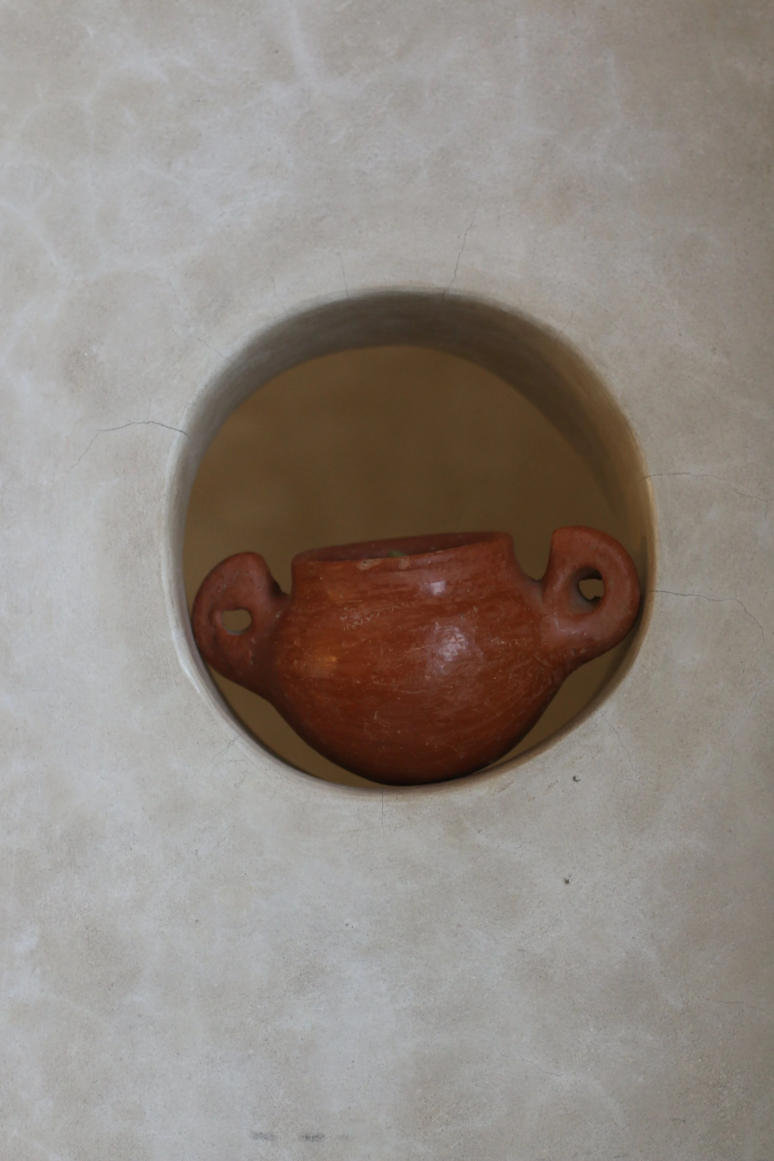 Une poterie en terre cuite rouge dans une alcôve creusée dans une surface beige.