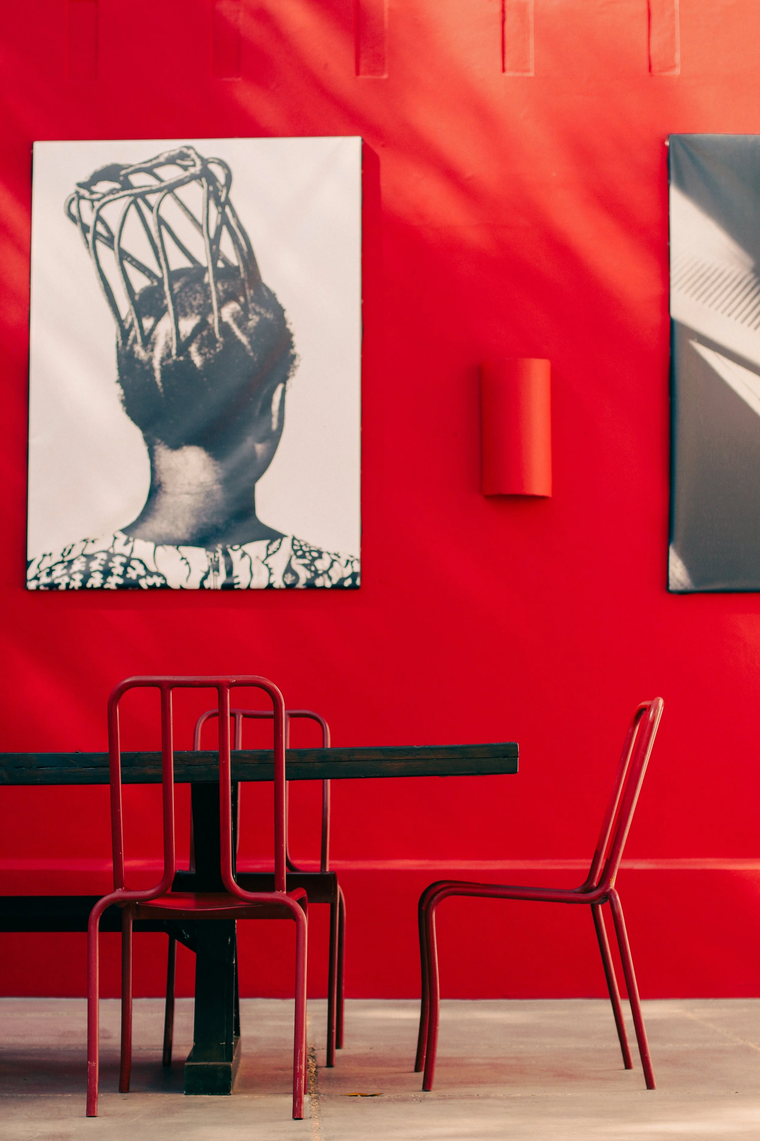 Intérieur avec mur rouge, deux tableaux modernes, une table noire et deux chaises rouges, une au centre et une à droite.