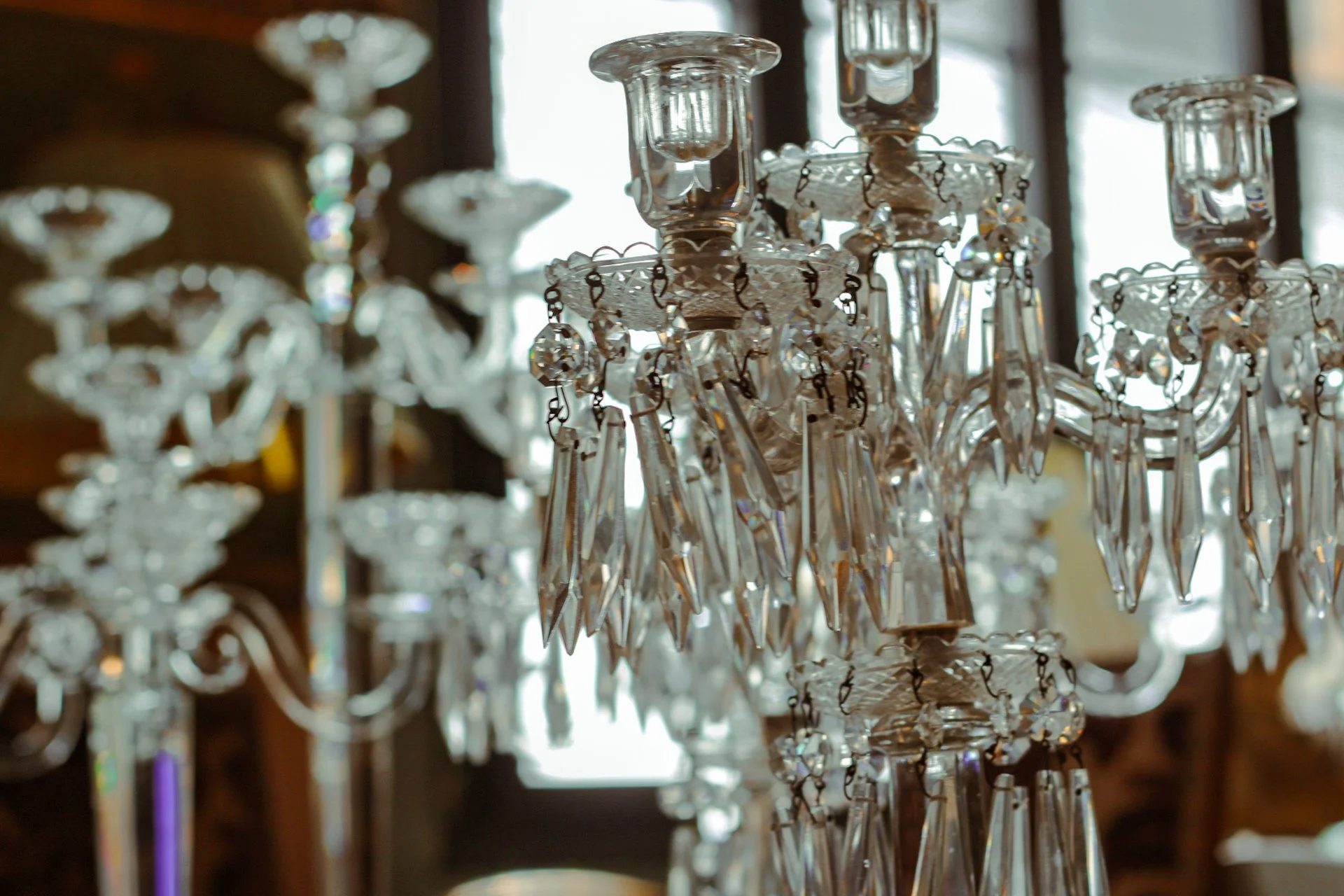 Un chandelier en cristal avec de nombreux pendentifs suspendus, dans une pièce éclairée par une grande fenêtre en arrière-plan.